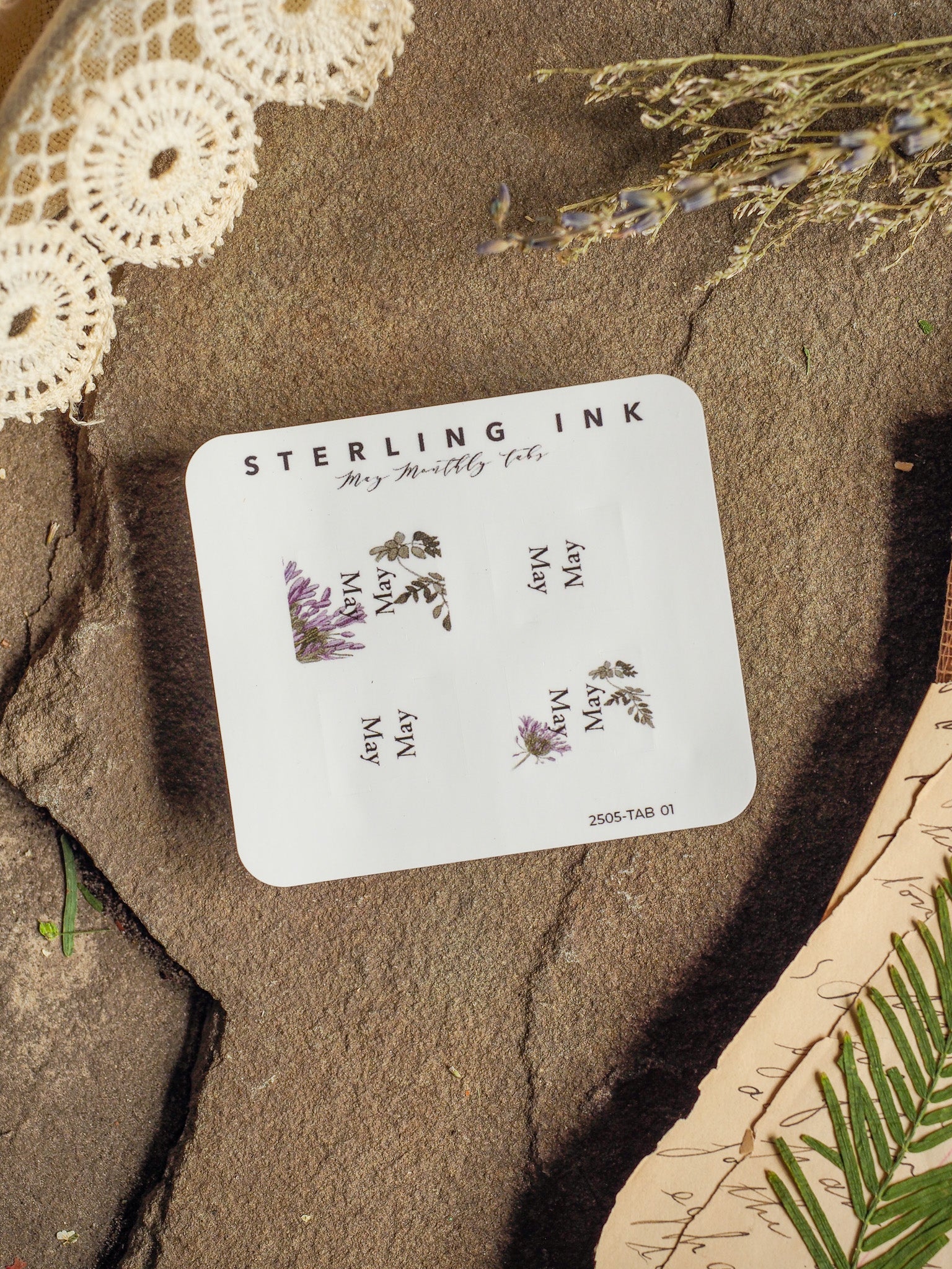 White planner card displaying "STERLING INK" and "May Monthly Tabs," featuring repeated text and delicate purple floral illustrations for journaling or organizational use.