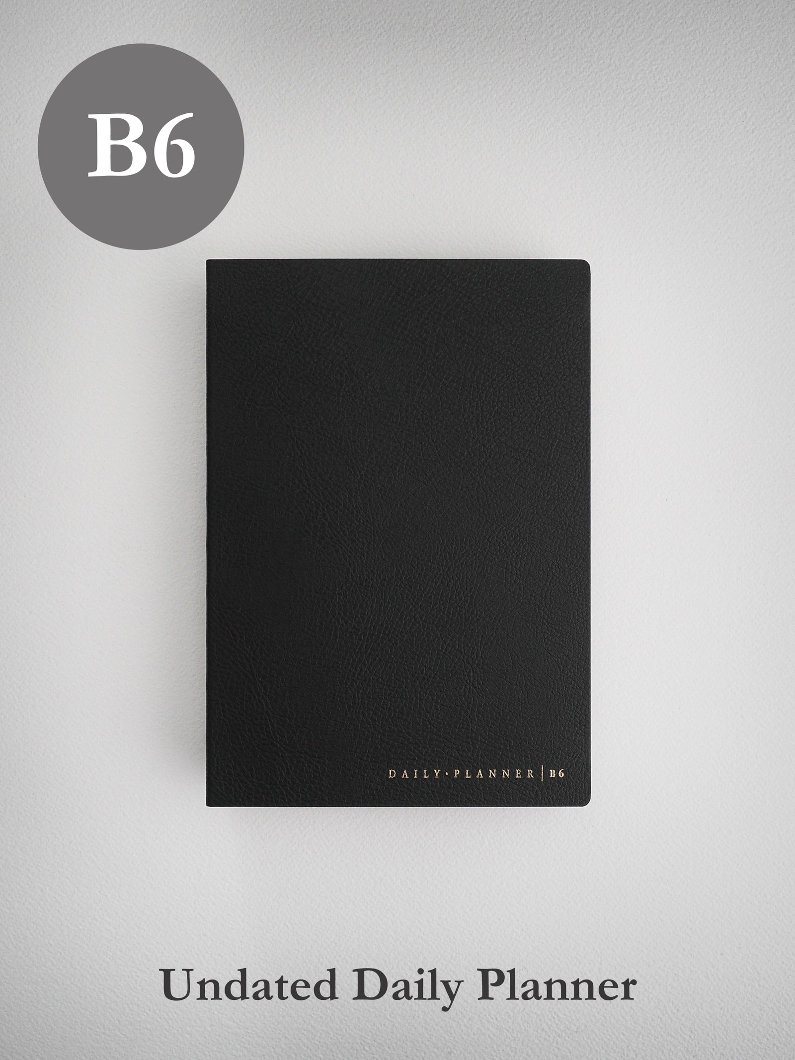 A matte black B6 daily planner journal featuring a structured, textured cover and subtle gold-toned branding near the bottom.