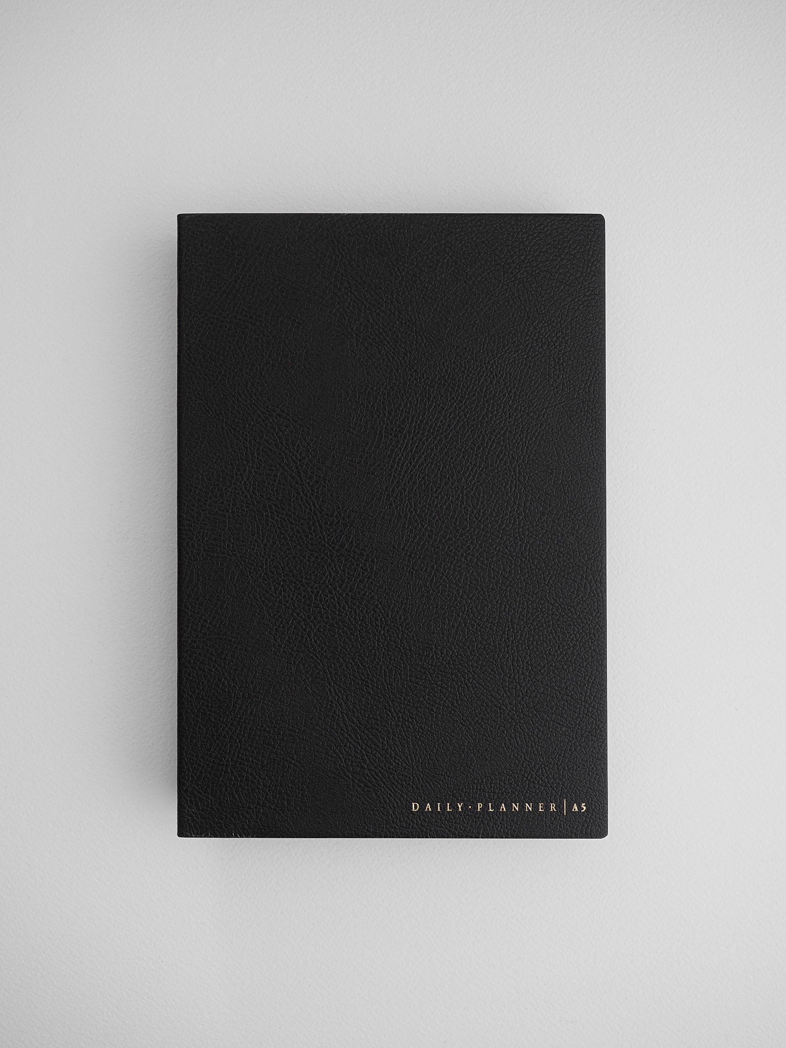 Elegant black A5 daily planner journal with a matte, textured cover, featuring subtle gold metallic lettering that reads "DAILY PLANNER | A5".