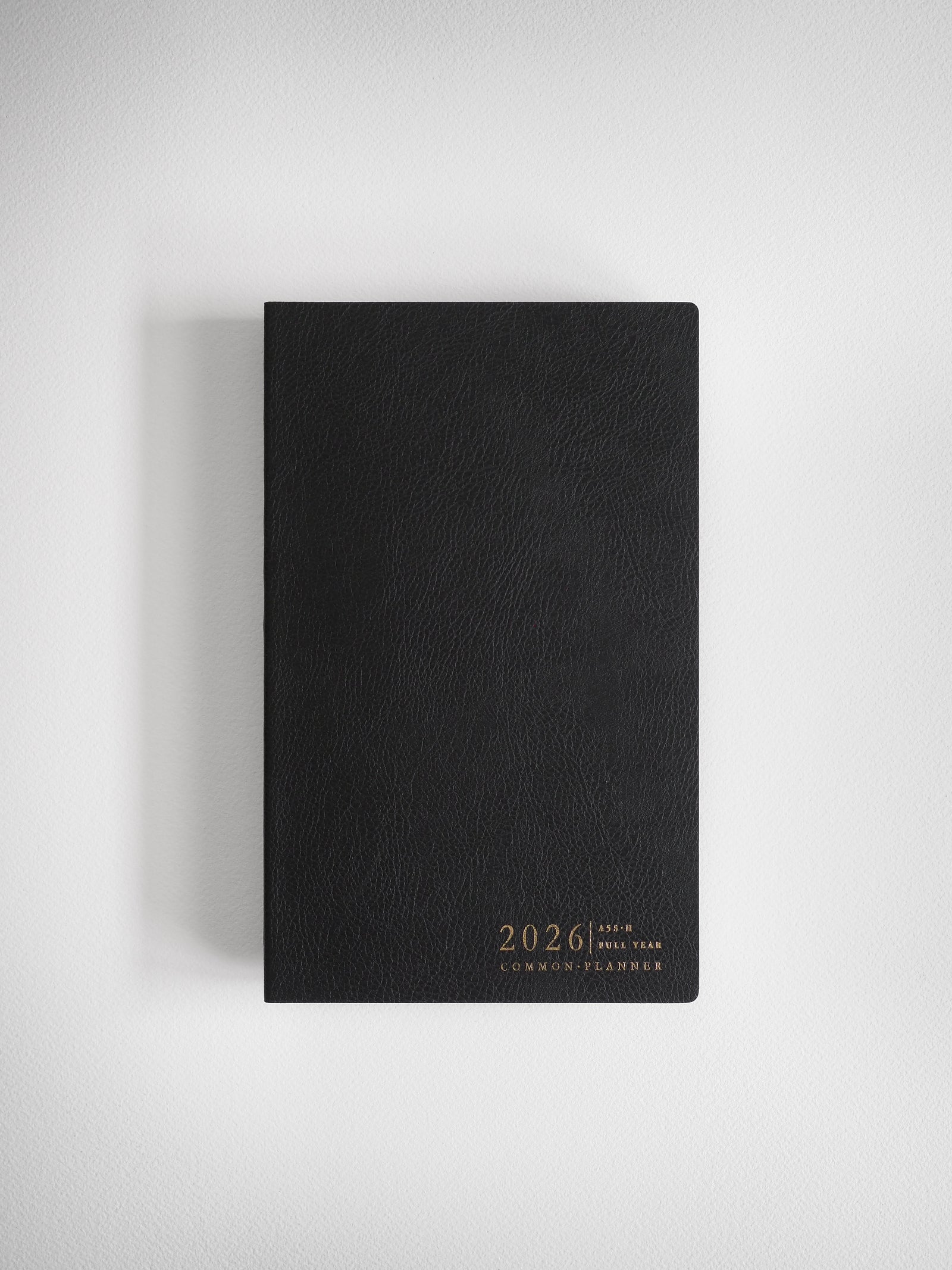 Elegant A5 planner with a matte black cover, featuring sophisticated gold foil stamping for "2026 Common Planner," ready for full-year organization.