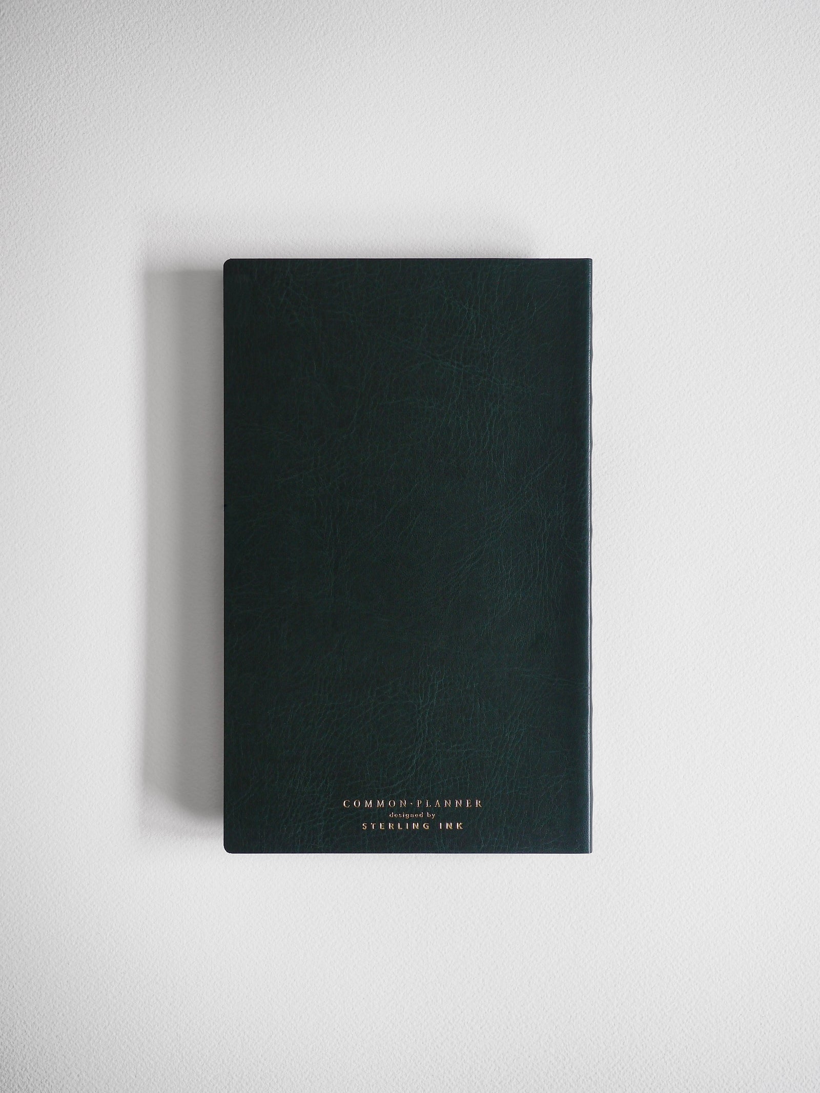 A dark, matte A5 slim planner featuring centered gold foil lettering that reads "COMMON PLANNER designed by STEERING INK."