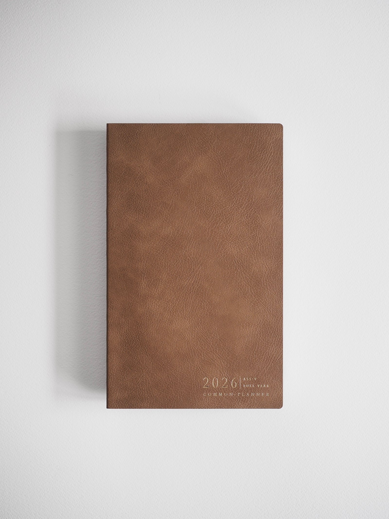 This elegant, warm brown A5 slim vertical planner features debossed gold lettering detailing the "2026 Common Planner" title.