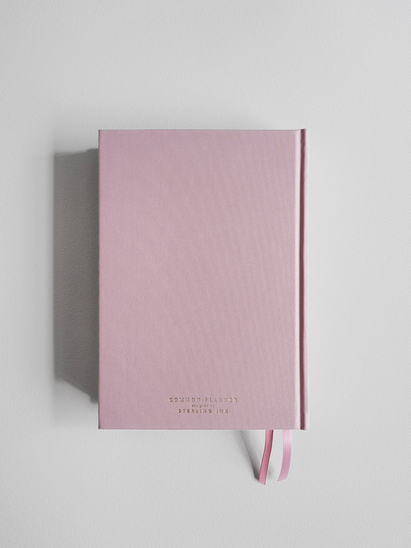 Soft blush pink A5 planner featuring centered "Common Planner" branding and a matching ribbon accent, ready for planning the full year.