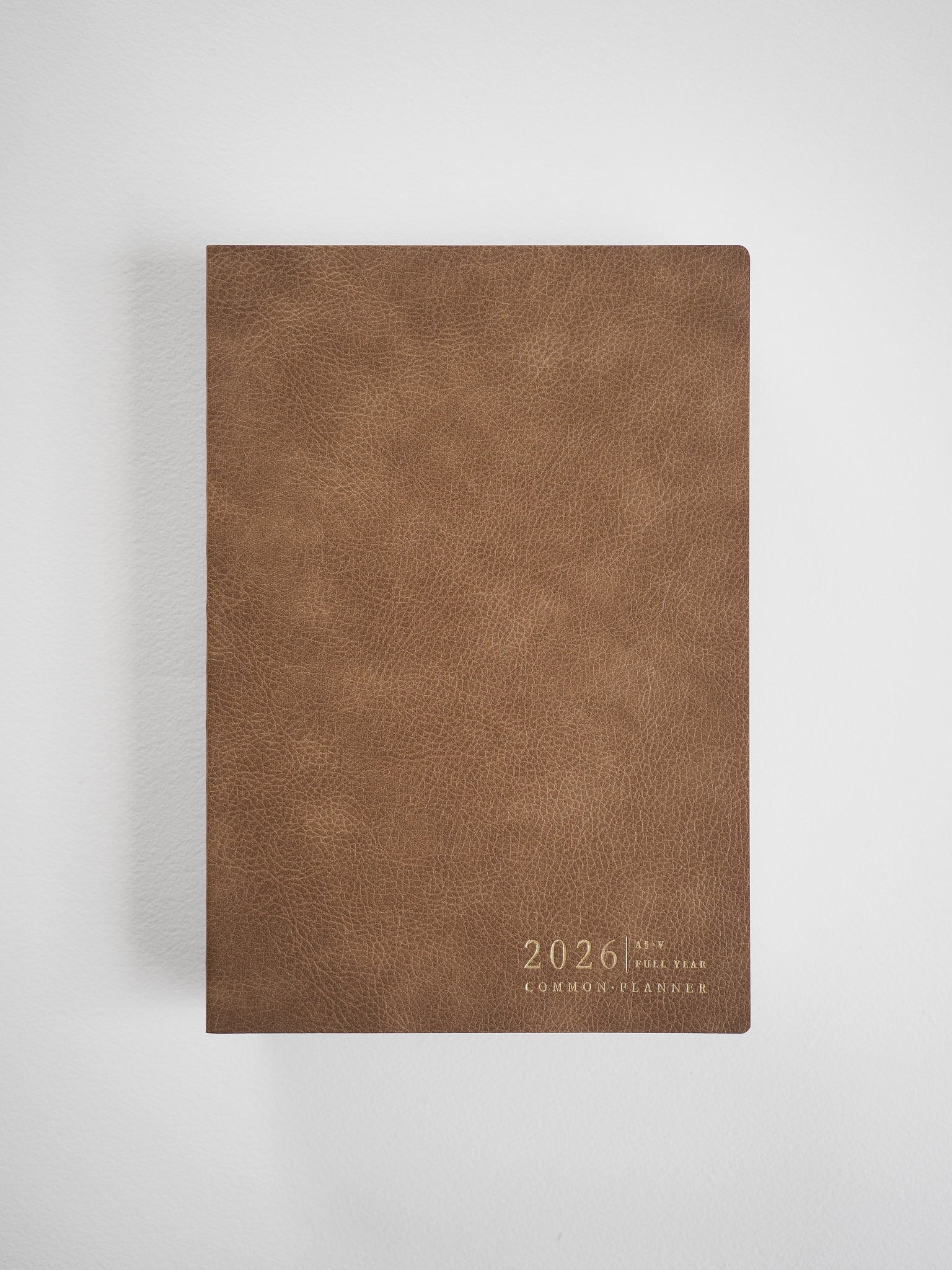 Vertical A5 planner cover crafted from textured, rich brown faux leather, subtly engraved with "2026 Full Year Common Planner."