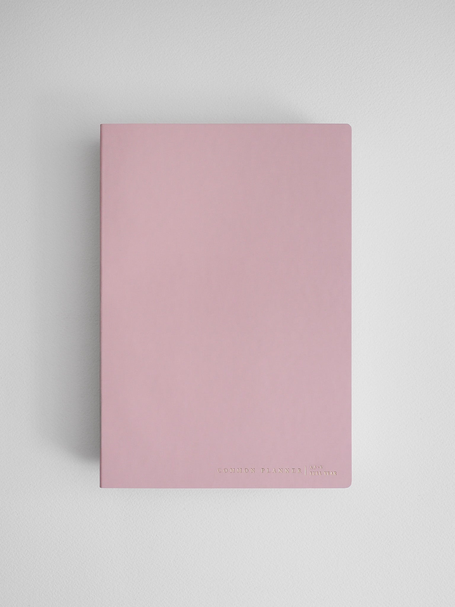 Minimalist dusty rose A5 vertical planner notebook featuring a solid pale pink cover and debossed text reading "Common Planner | Full Year."