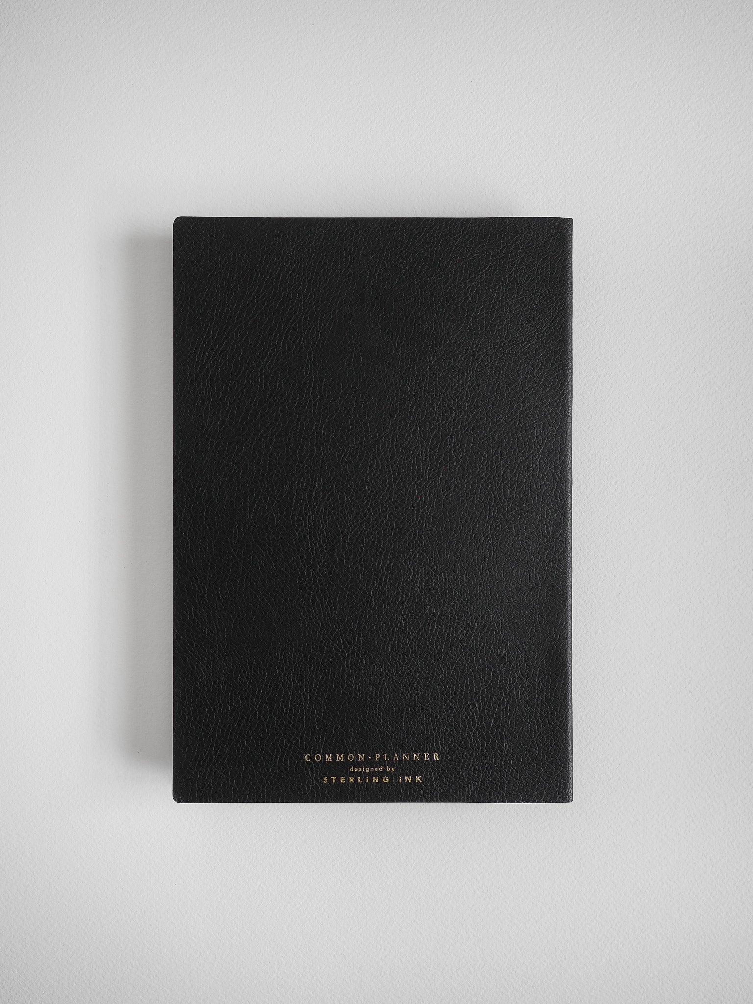 Black A5 common planner journal with faux leather binding, featuring elegant foiled text that reads "COMMON PLANNER designed by STERLING INK."