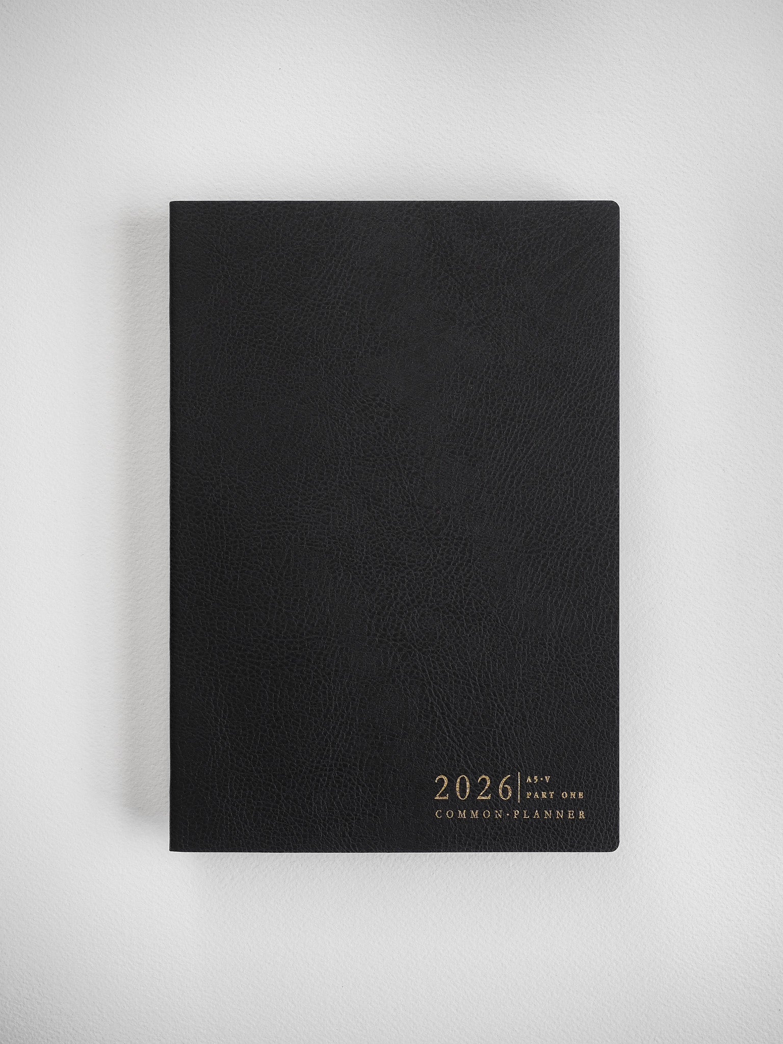 Minimalist black A5 planner with a smooth cover, featuring the centered gold-toned branding "2026 Common Planner" for organization.