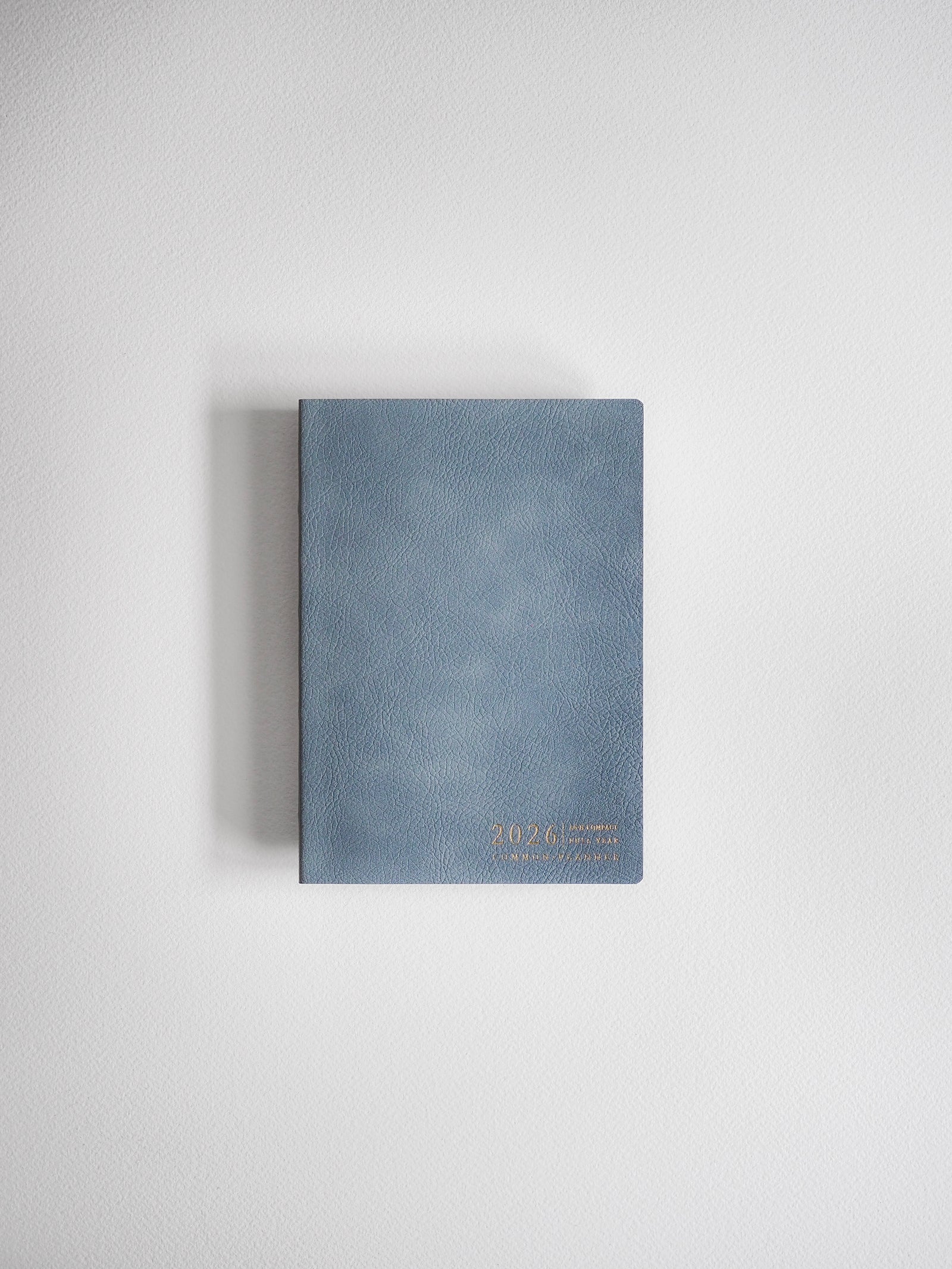 Elegant A6 horizontal planner in a muted blue-gray shade, featuring minimal metallic gold lettering that indicates the 2026 academic year.