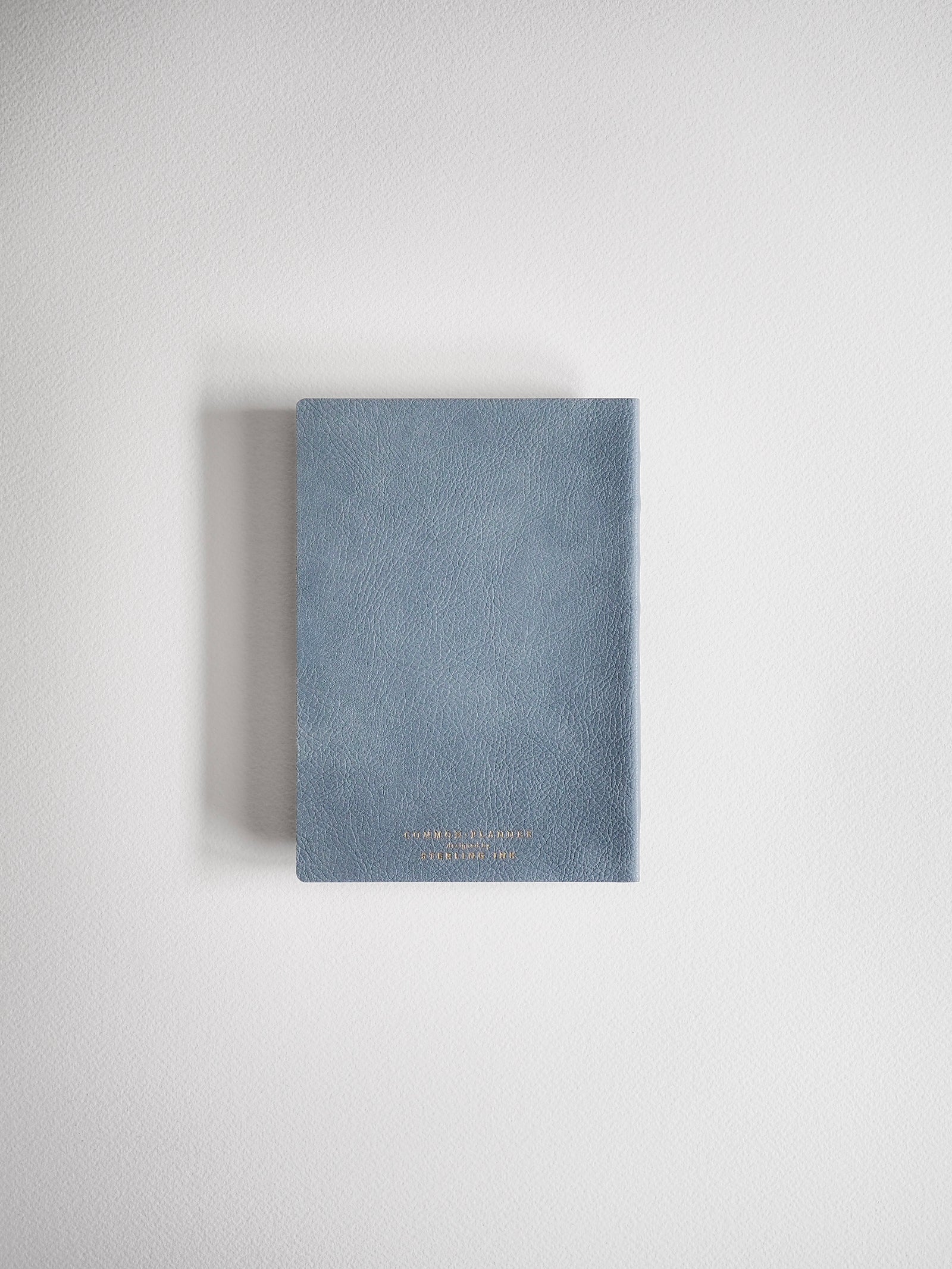 This A6 compact full-year planner features a muted blue-gray hardcover and includes minimal gold-colored branding identifying the 2026 collection on the front.