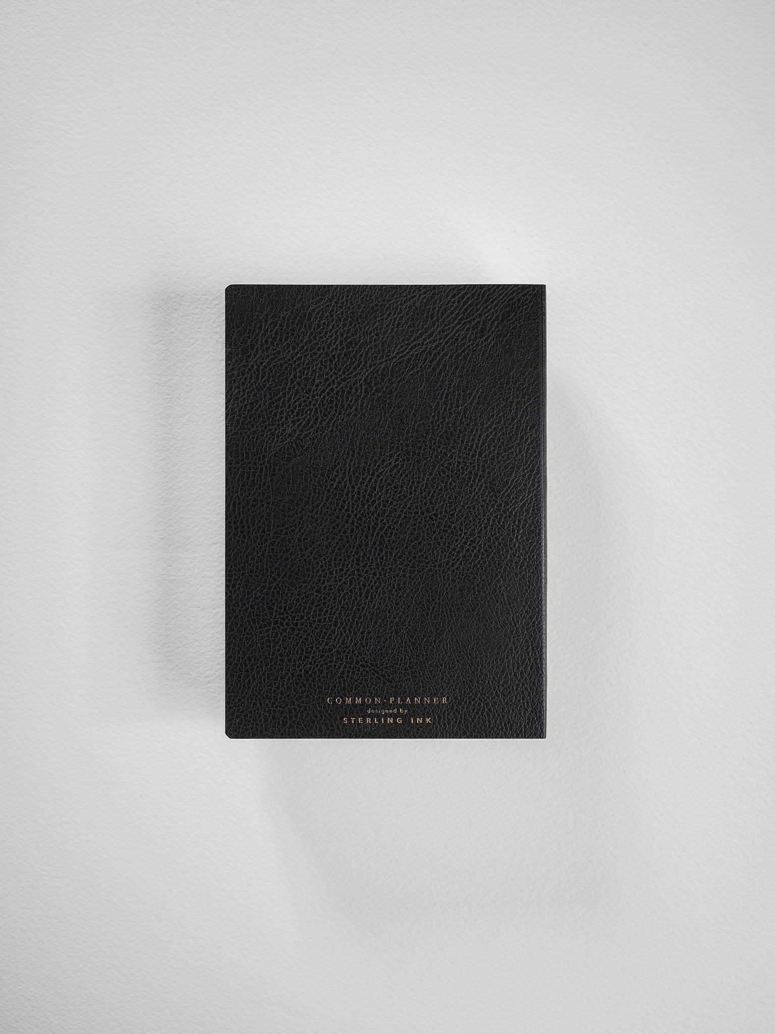 A black, A6 horizontal Common Planner featuring a textured faux leather cover and subtle gold-toned branding for the 2026 year.