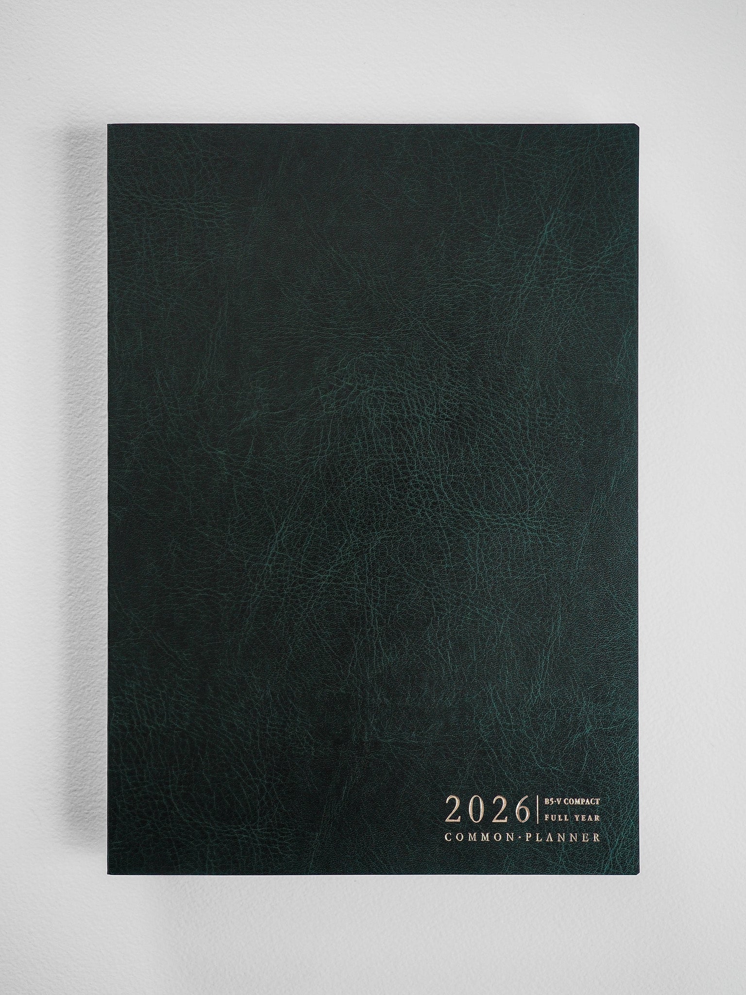 Deep slate green planner cover with a textured faux leather finish and centered gold foil debossing of the 2026 date and common planner title.
