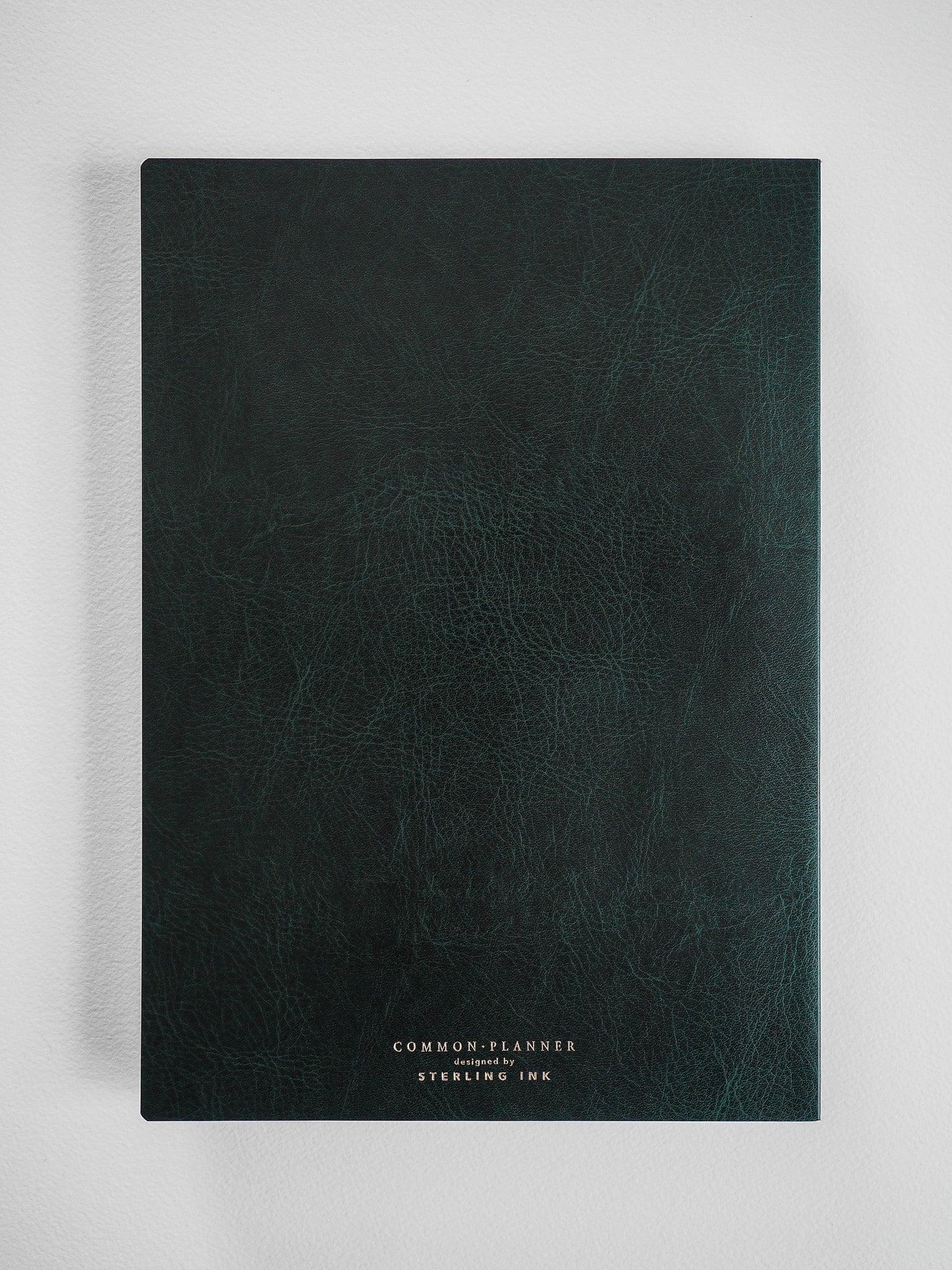 Deep, textured dark emerald green planner featuring centered white branding that reads "COMMON PLANNER designed by STERLING INK."