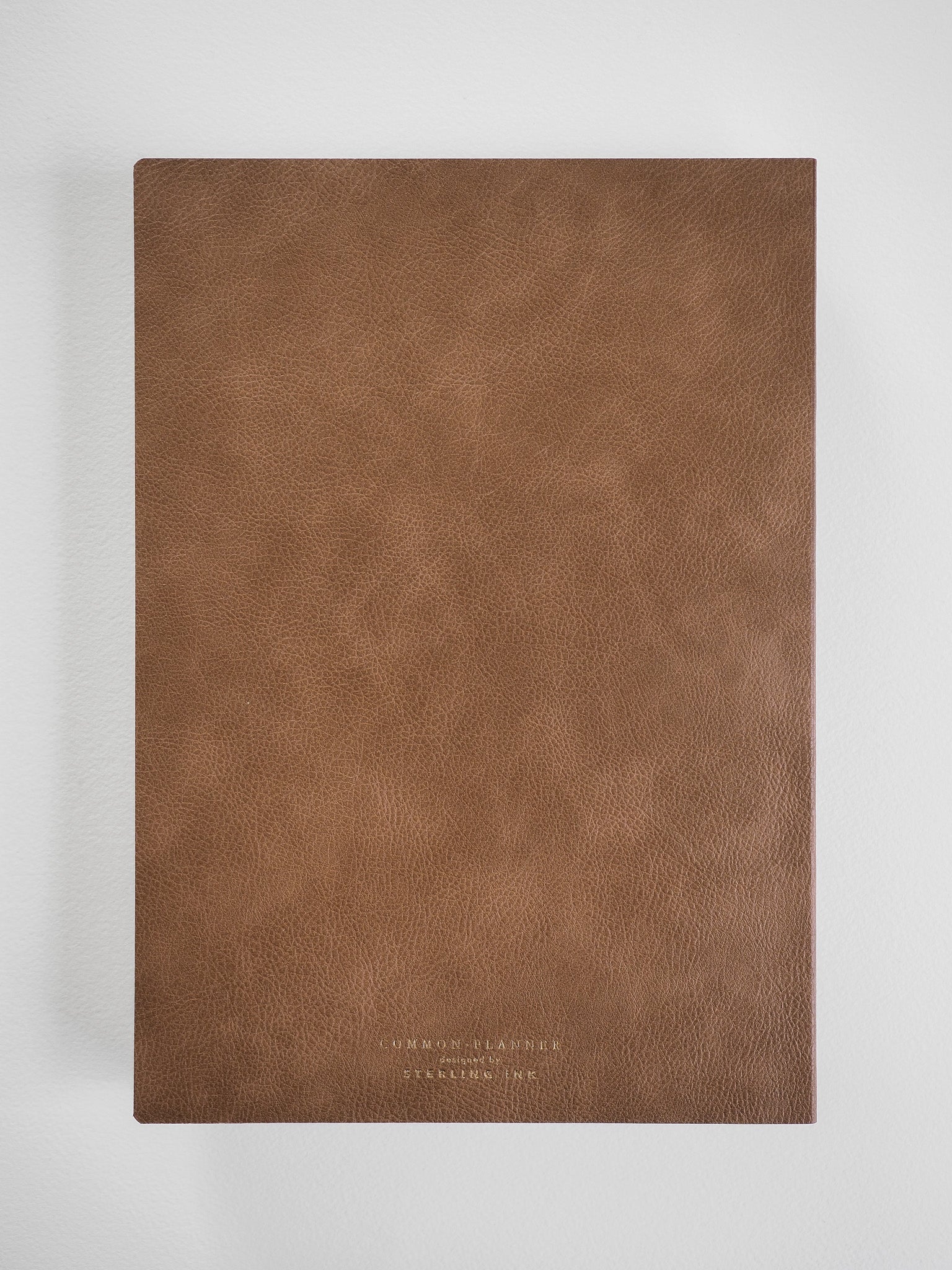A textured, rich mocha brown faux leather planner cover featuring minimalist debossed lettering for the Common Planner 2026 journal.