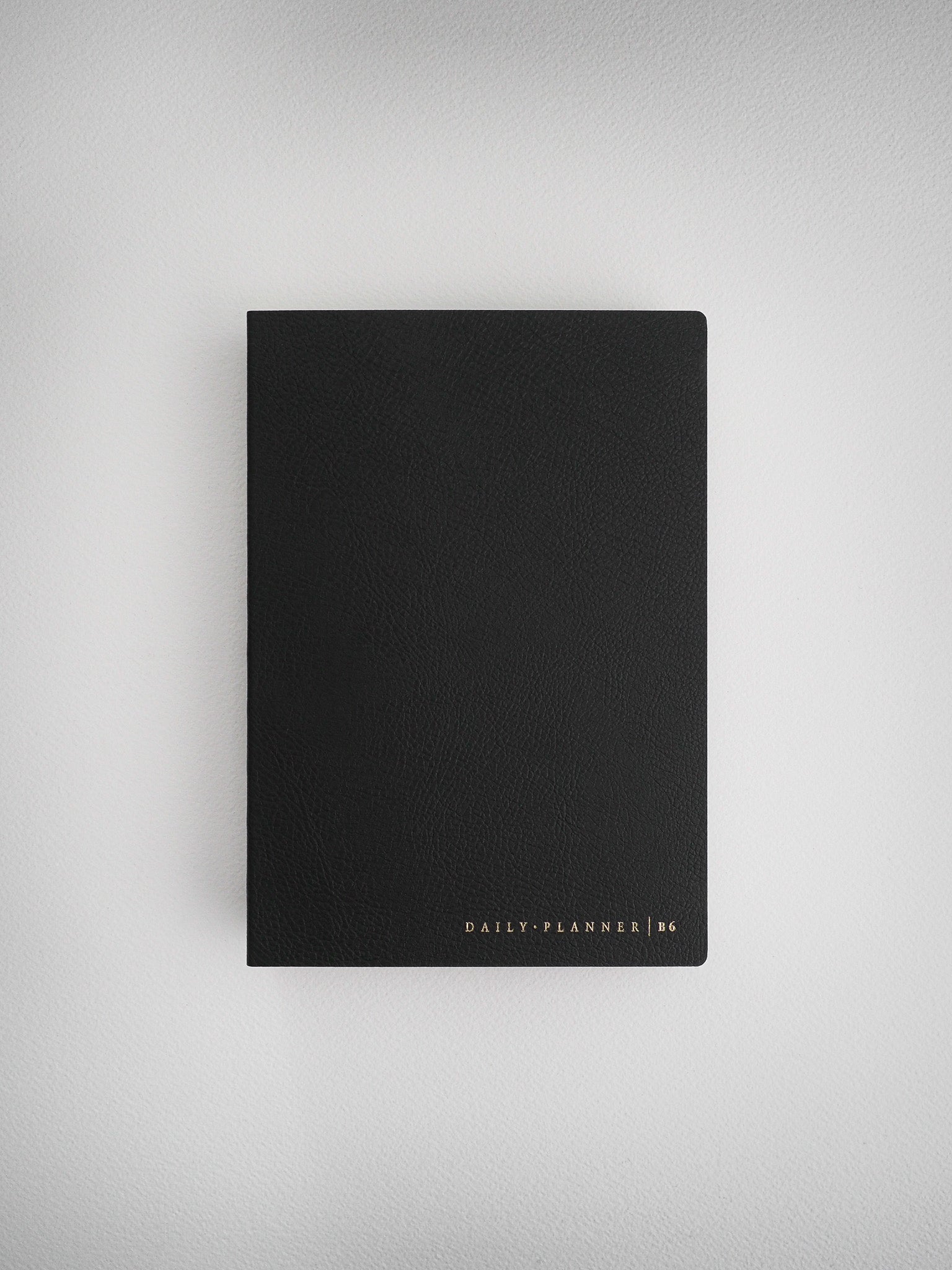 Sleek, solid black B6 daily planner notebook, featuring minimalist design and subtle metallic gold foil branding.