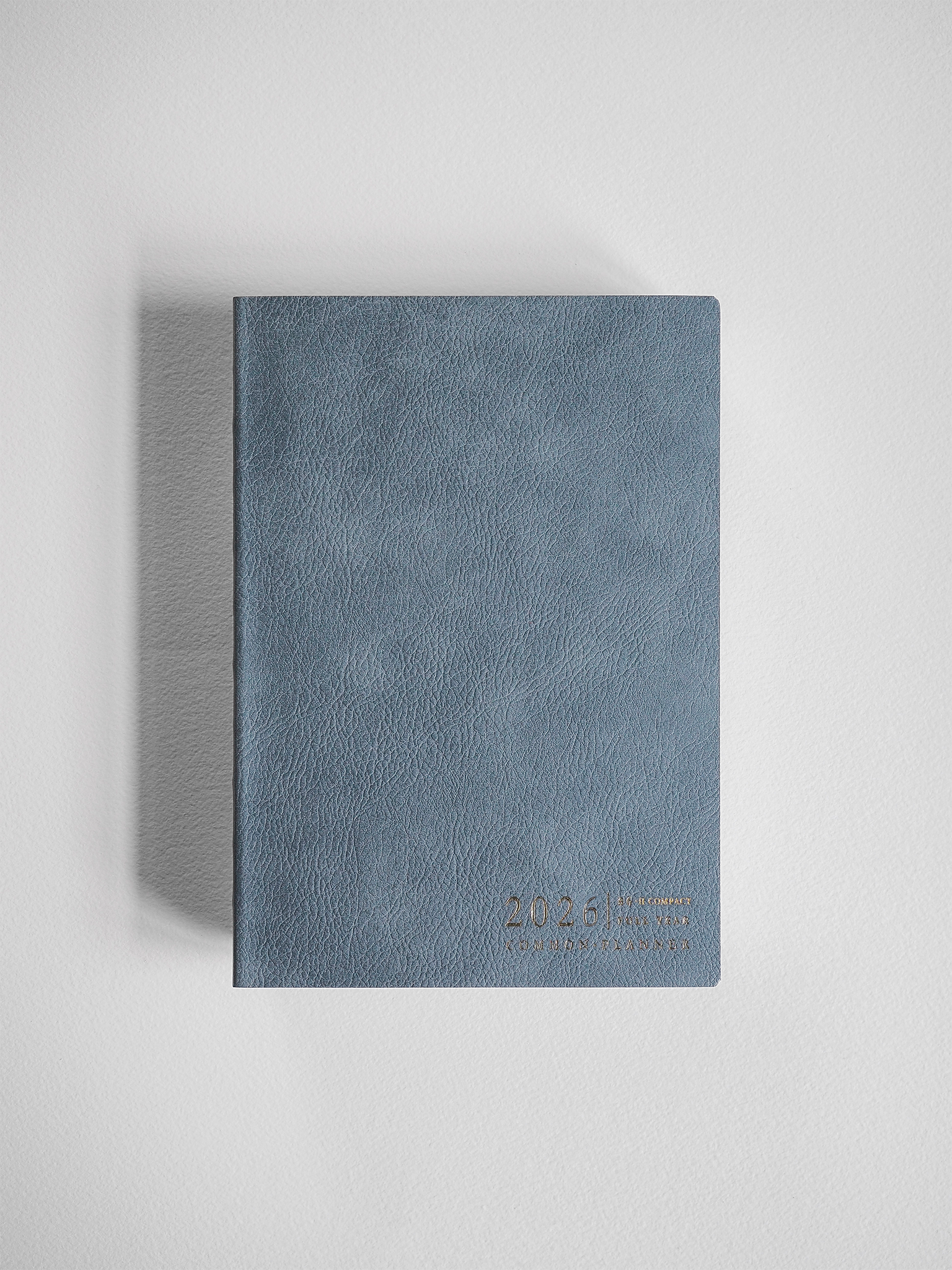 Slate blue, textured B6 planner for 2026, featuring a compact, horizontal format with subtle year branding printed near the bottom.