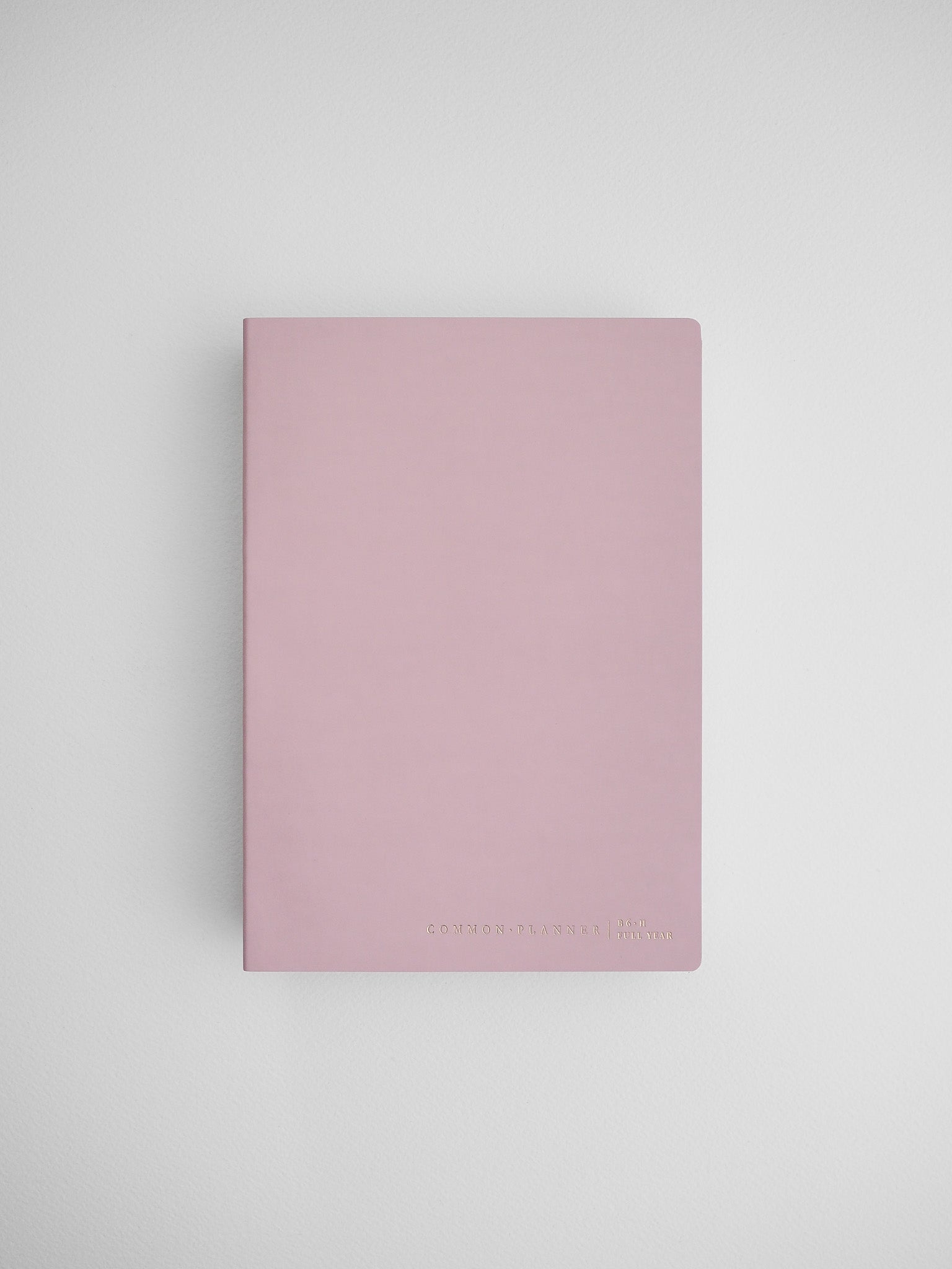 Blush pink B6 common planner notebook, featuring a minimalist design and subtle printed text for journaling or organization.
