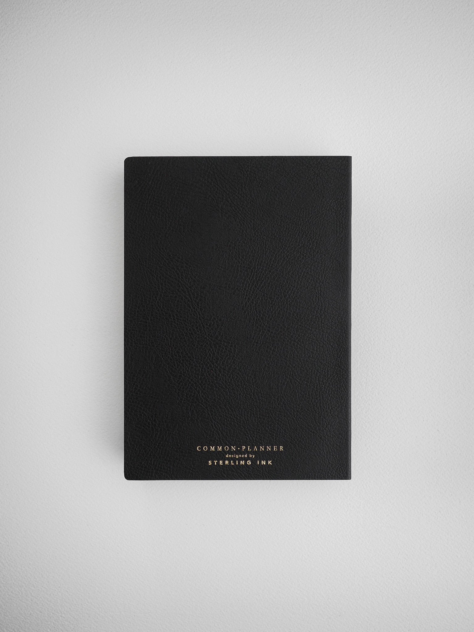 Sleek black planner notebook with a faux leather texture, featuring embossed gold lettering that reads "COMMON PLANNER designed by STERLING INK."