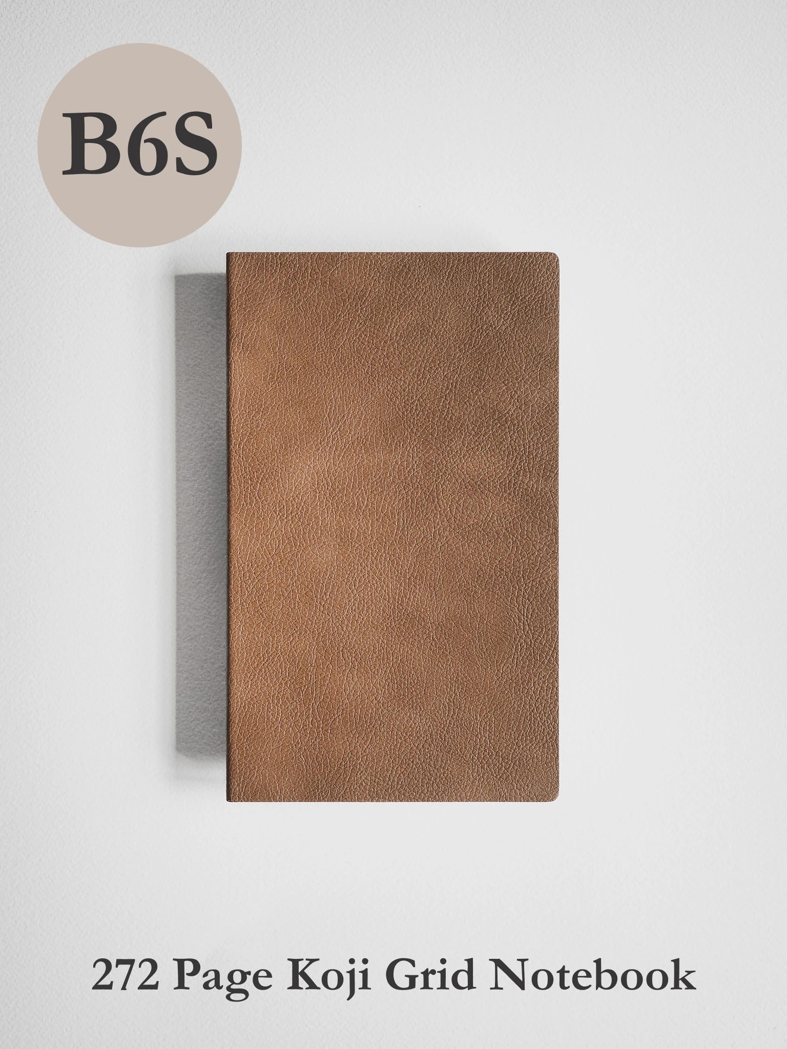 A brown textured notebook cover shown closed on a light gray background, with a beige circle label reading 'B6S' at the top left and text at the bottom reading '272 Page Koji Grid Notebook'.
#Color_Caramel