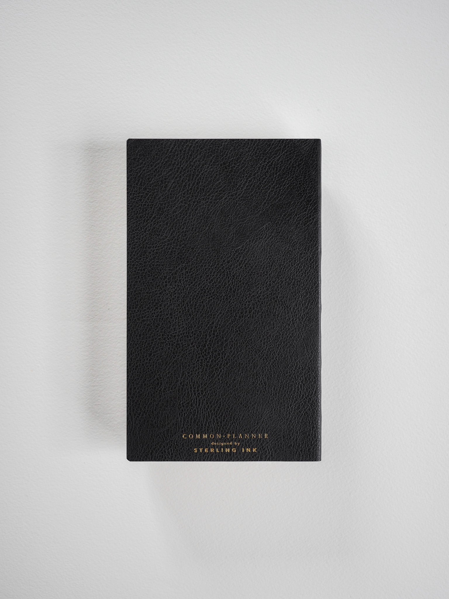 Elegant, black planner featuring a smooth, matte cover and centered gold foil lettering that reads 'COMMON PLANNER' and the brand name.