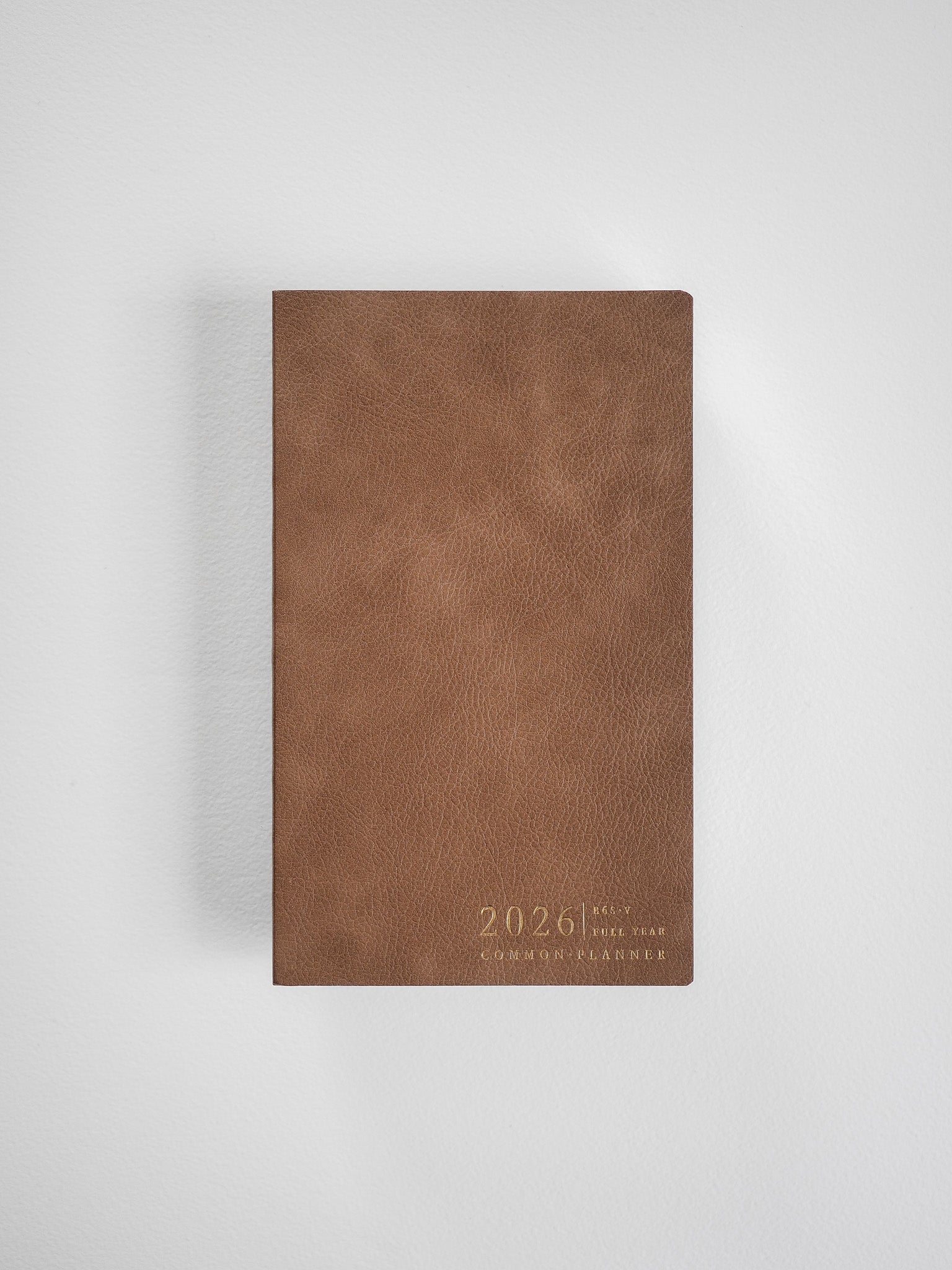 A slim, full-year 2026 planner featuring a matte, rich tan cover with "Common Planner" embossed text near the bottom.