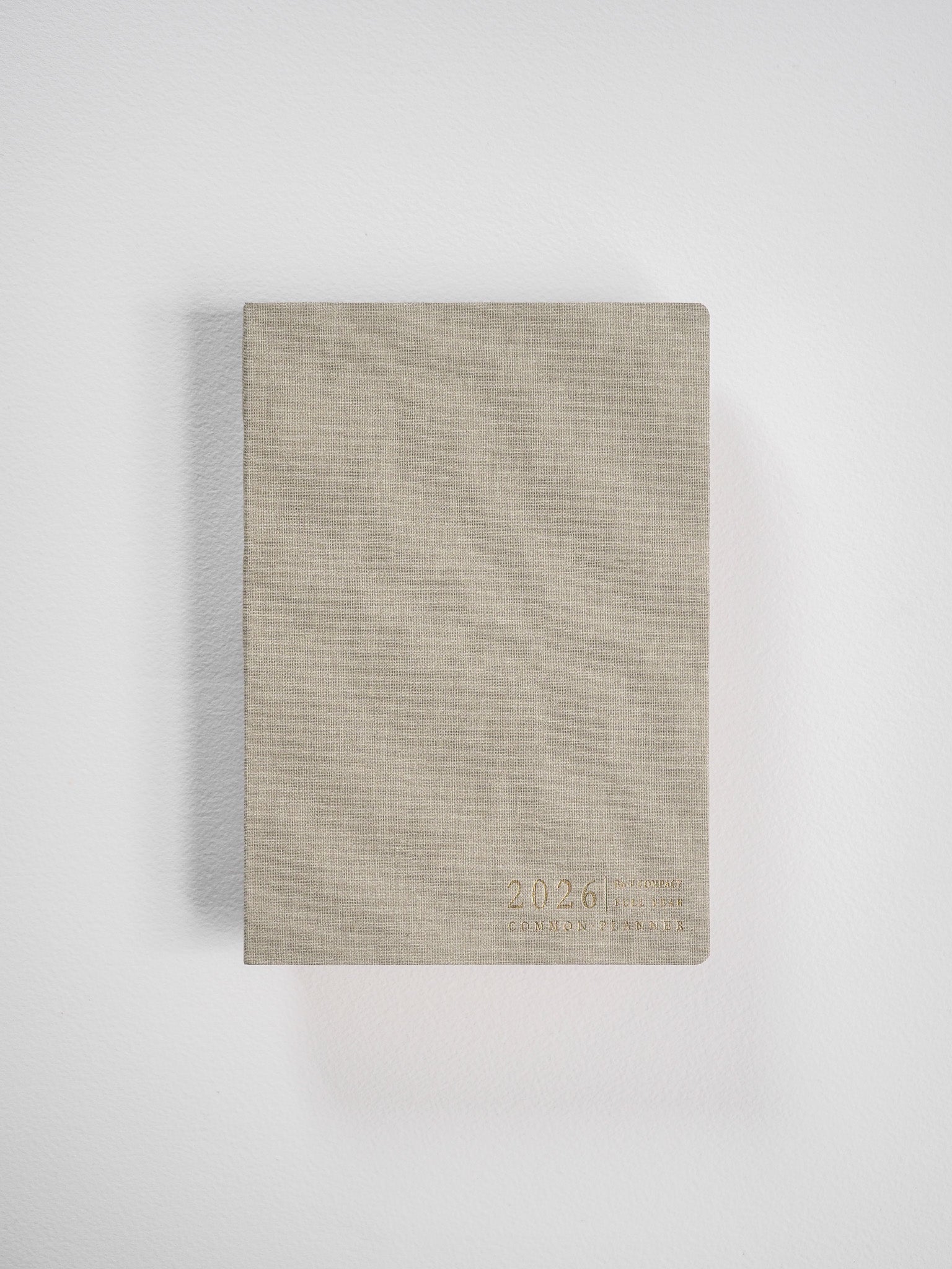 Compact B6 vertical planner with a textured beige cover, featuring subtle, minimalist debossed lettering for "2026 Common Planner."