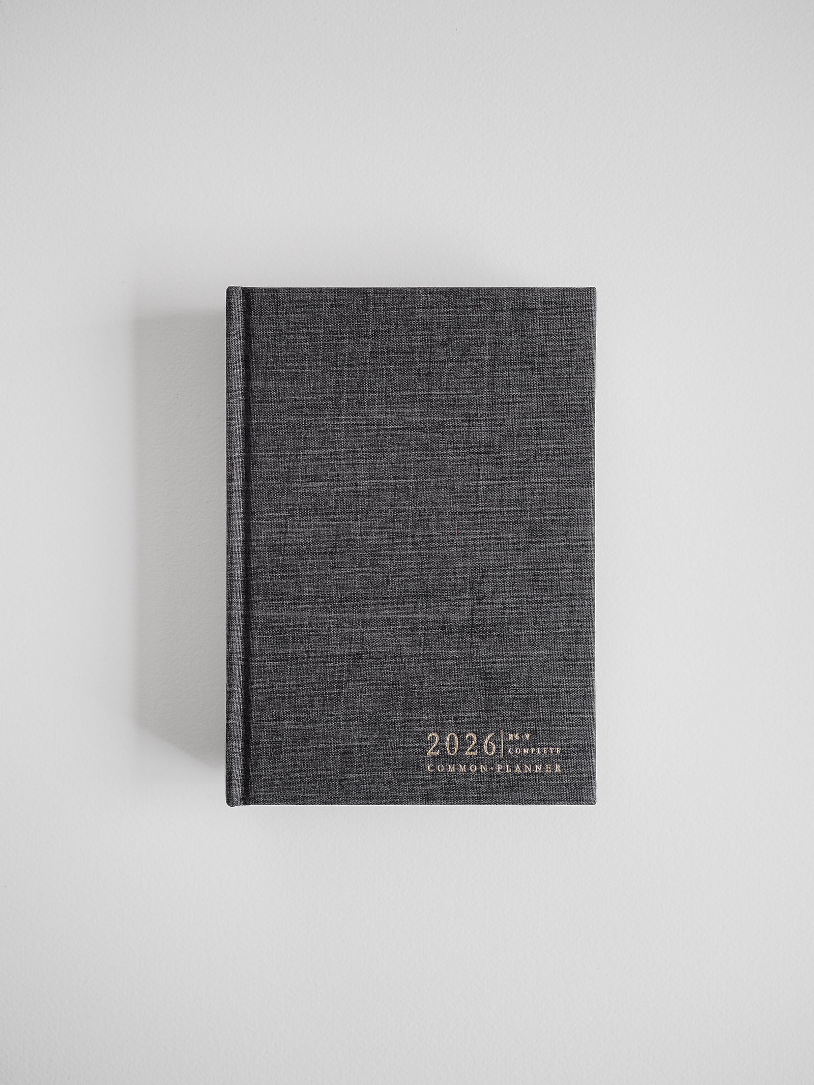 A dark charcoal B6 planner bound in textured material, featuring the embossed and centered title "2026 Common Planner" on the front cover.