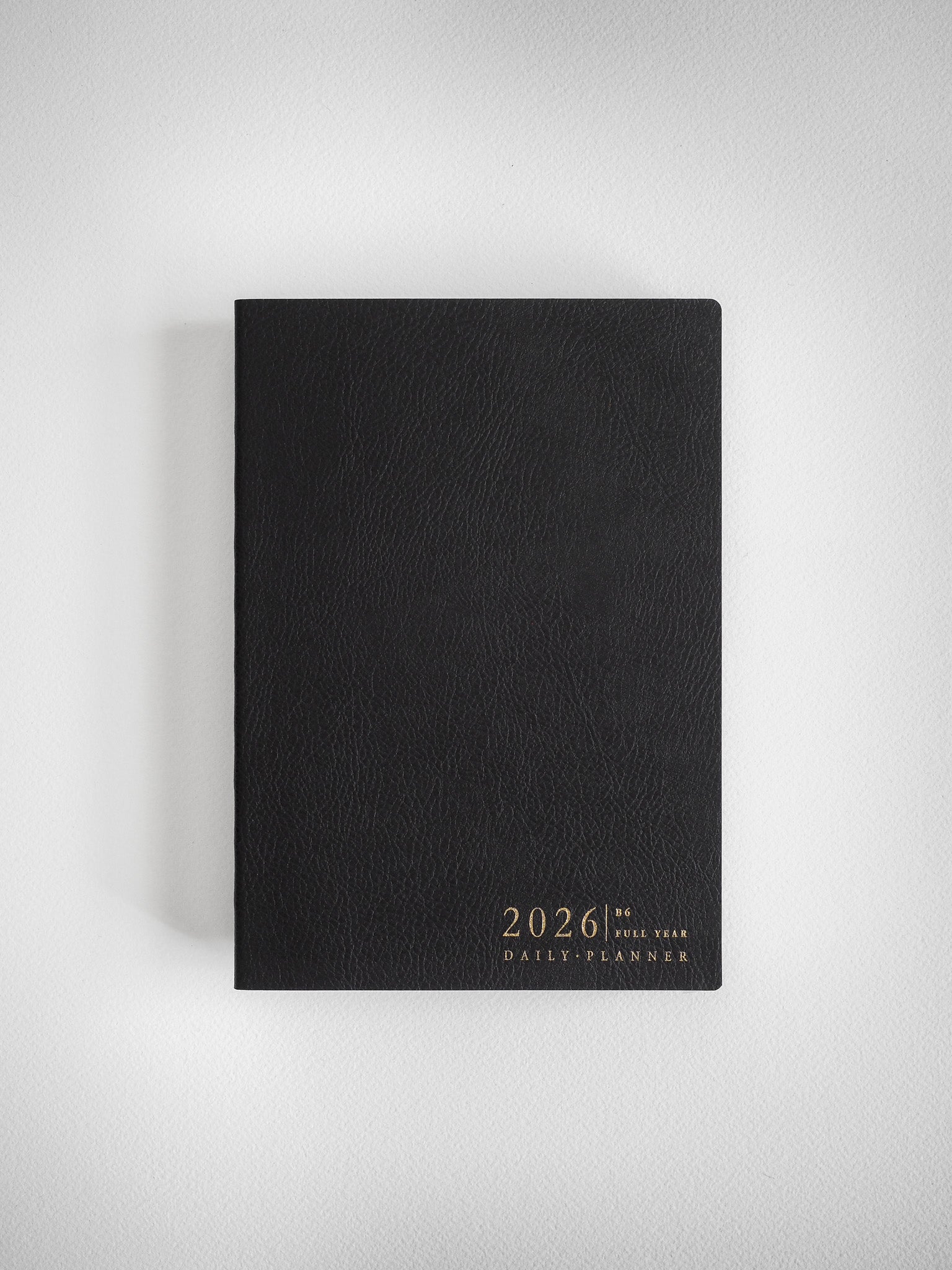 Sleek black B6 daily planner featuring elegant gold lettering that displays the year 2026 and "Full Year Daily Planner."