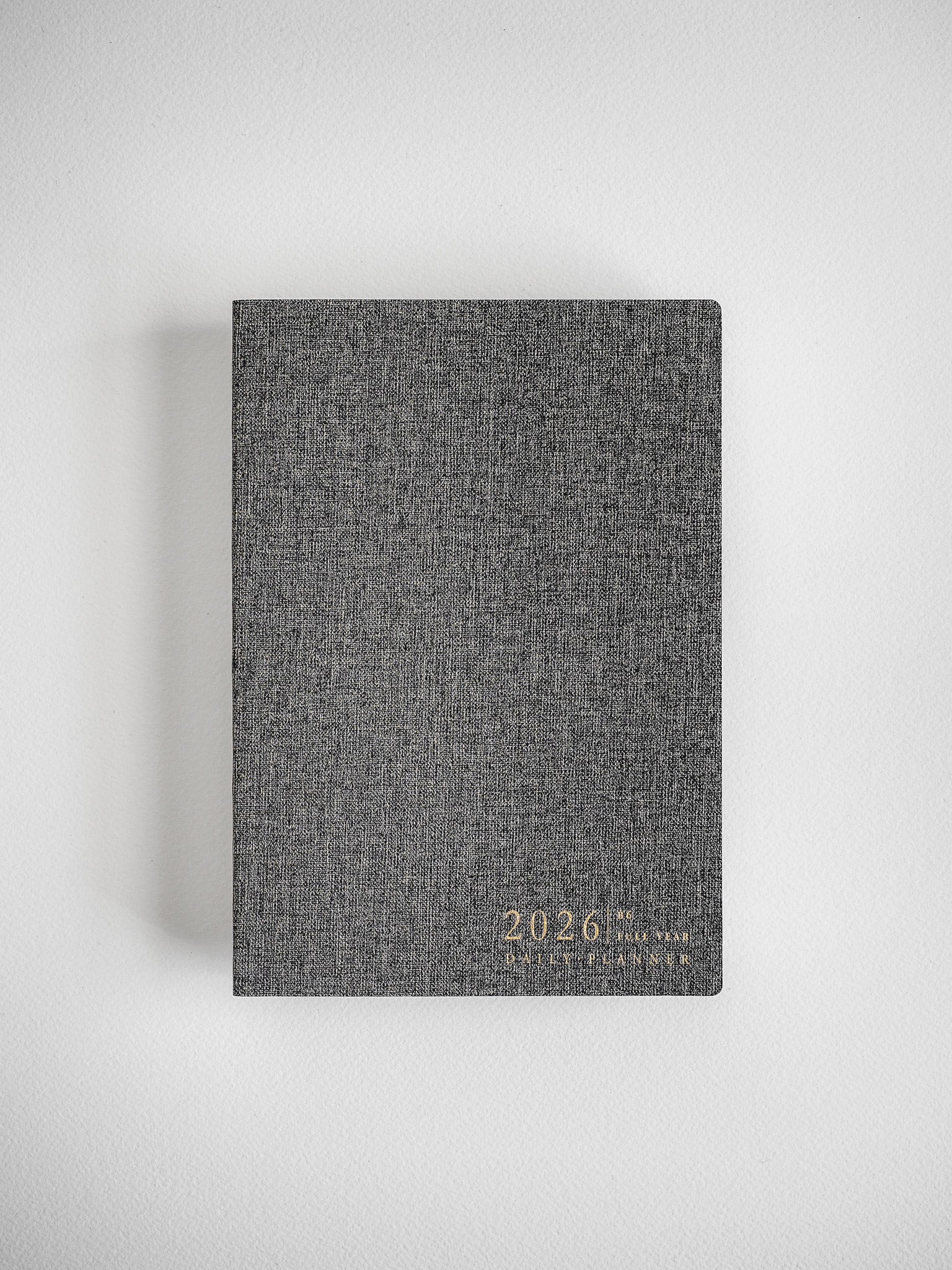 Dark gray, textured B6 daily planner for 2026, featuring elegant gold foil lettering displaying the year and planner title.
