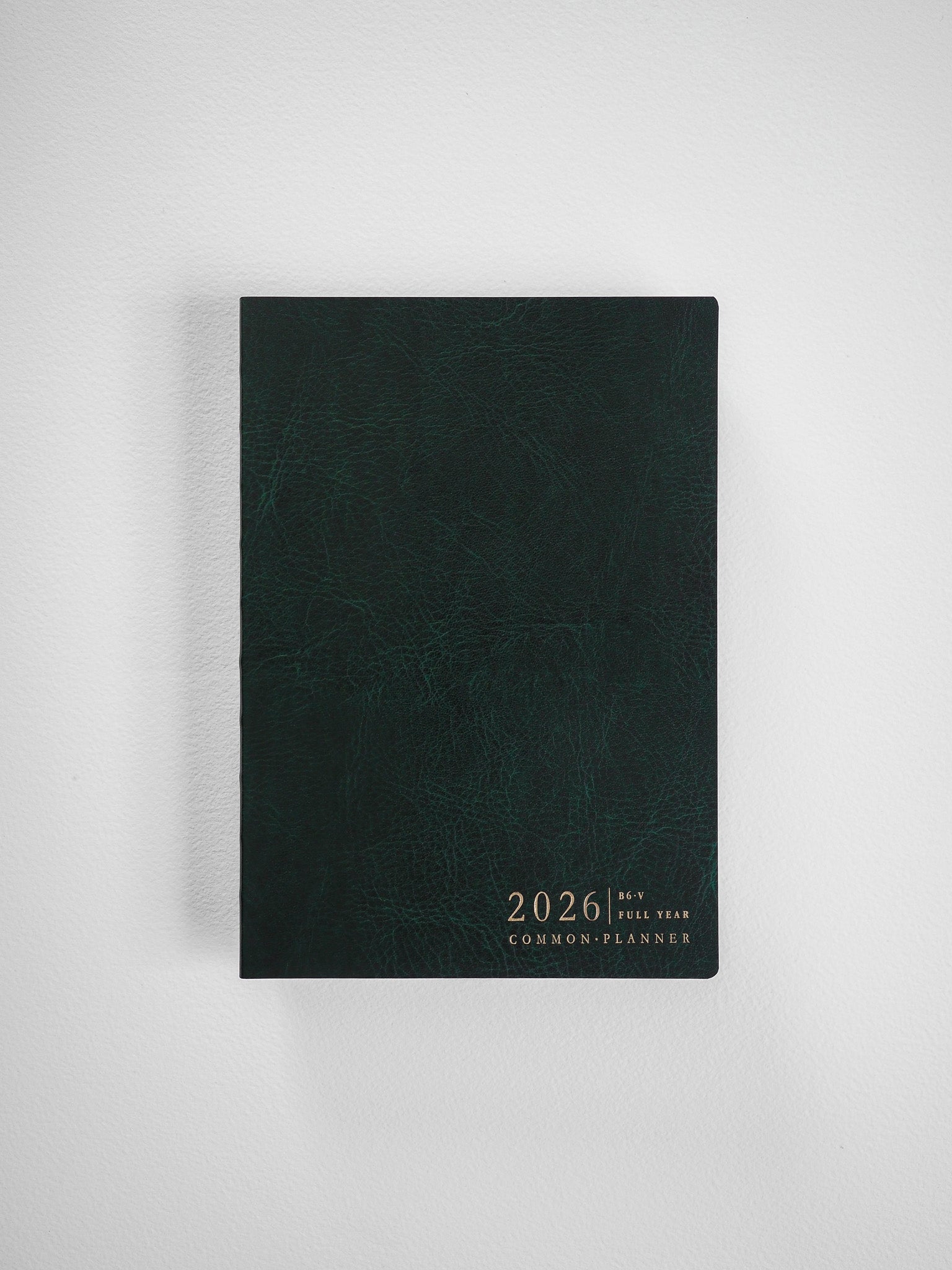 Deep forest green planner with a textured, faux leather cover, featuring centered gold lettering that reads "2026 Full Year Common Planner."