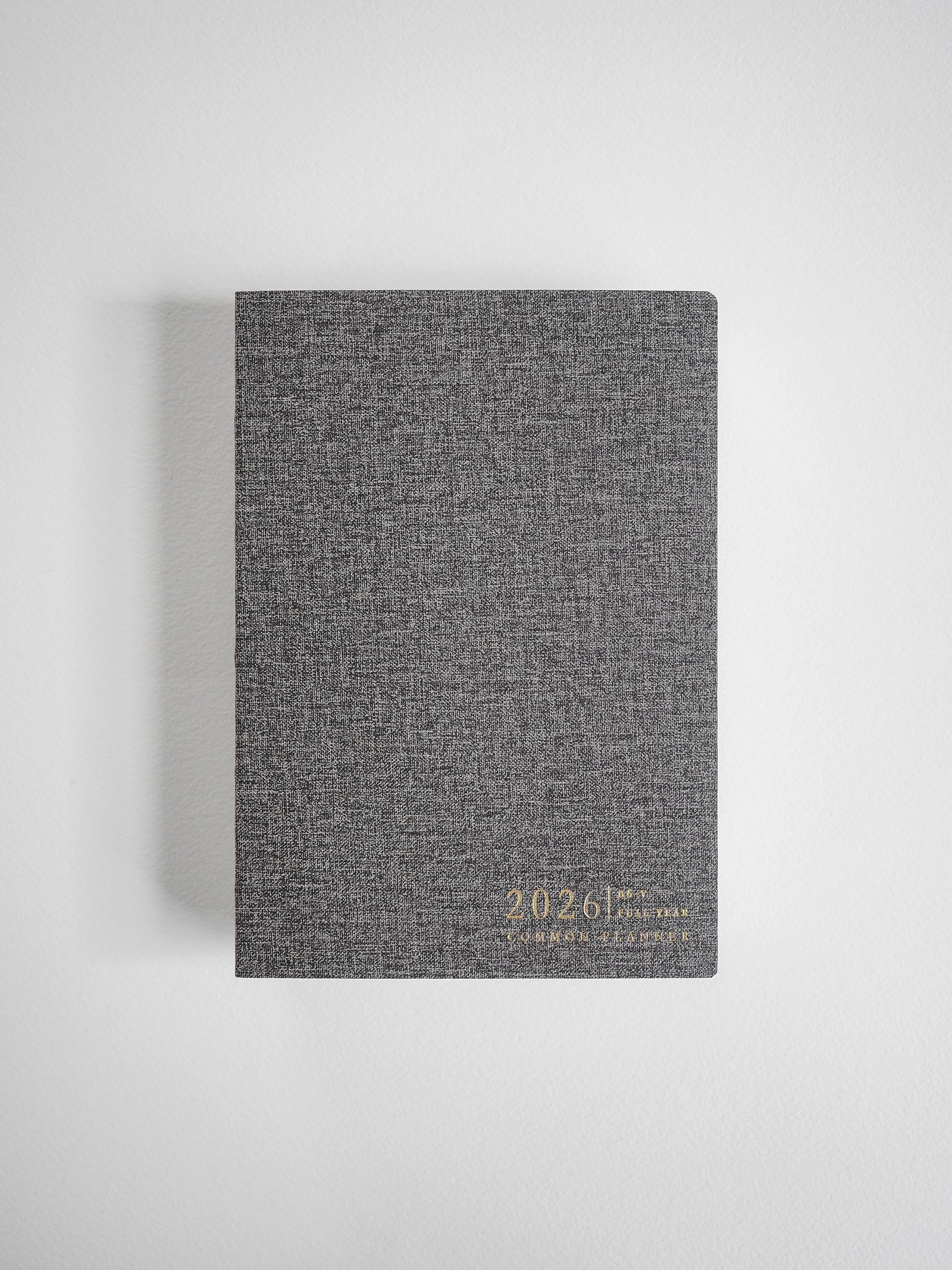Textured dark gray vertical planner featuring elegant gold foil embossing of the year 2026 on the cover.