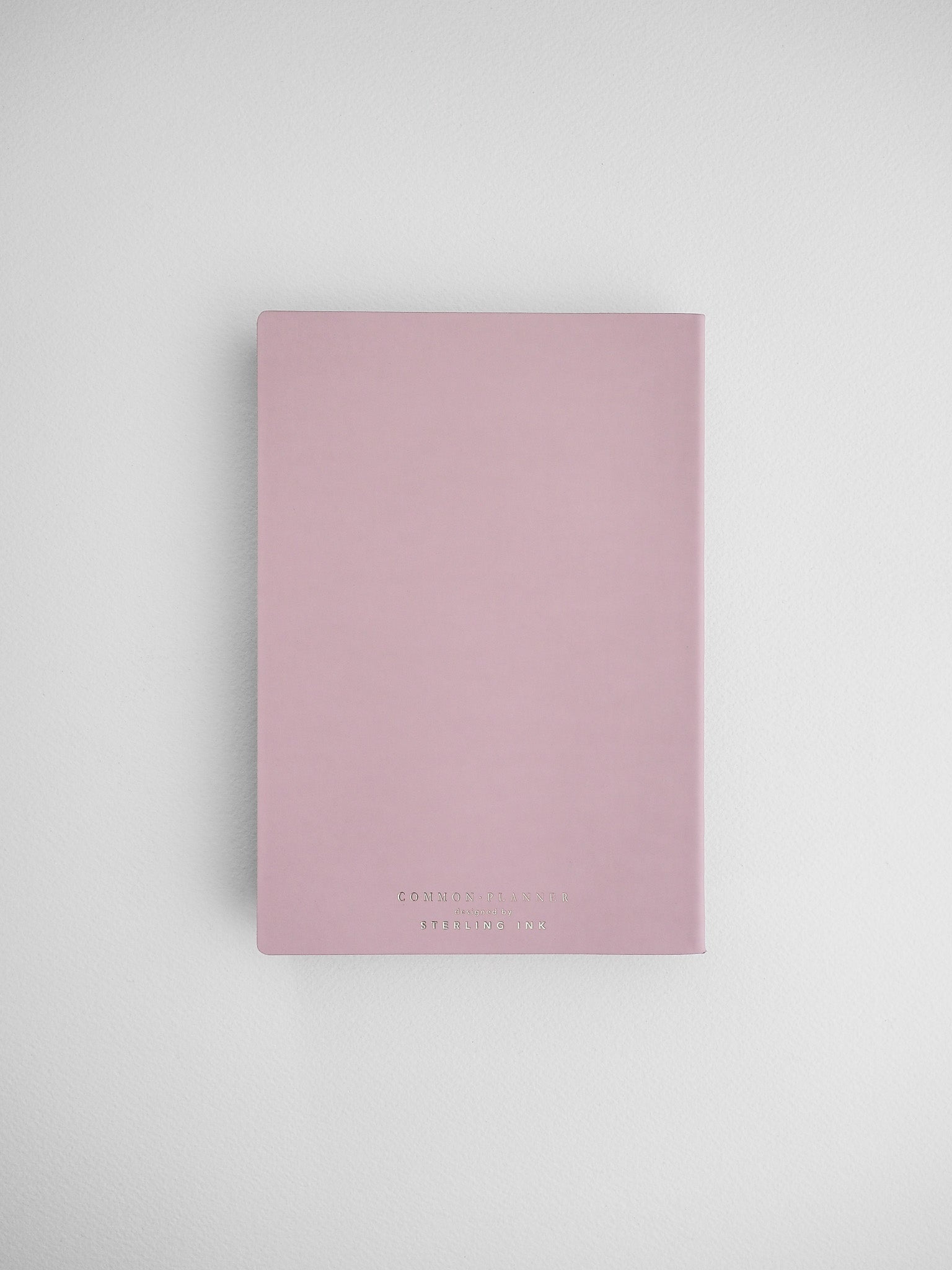 Blush pink vertical planner notebook featuring subtle, elegant black lettering that displays the title "Common Planner" on the front cover.