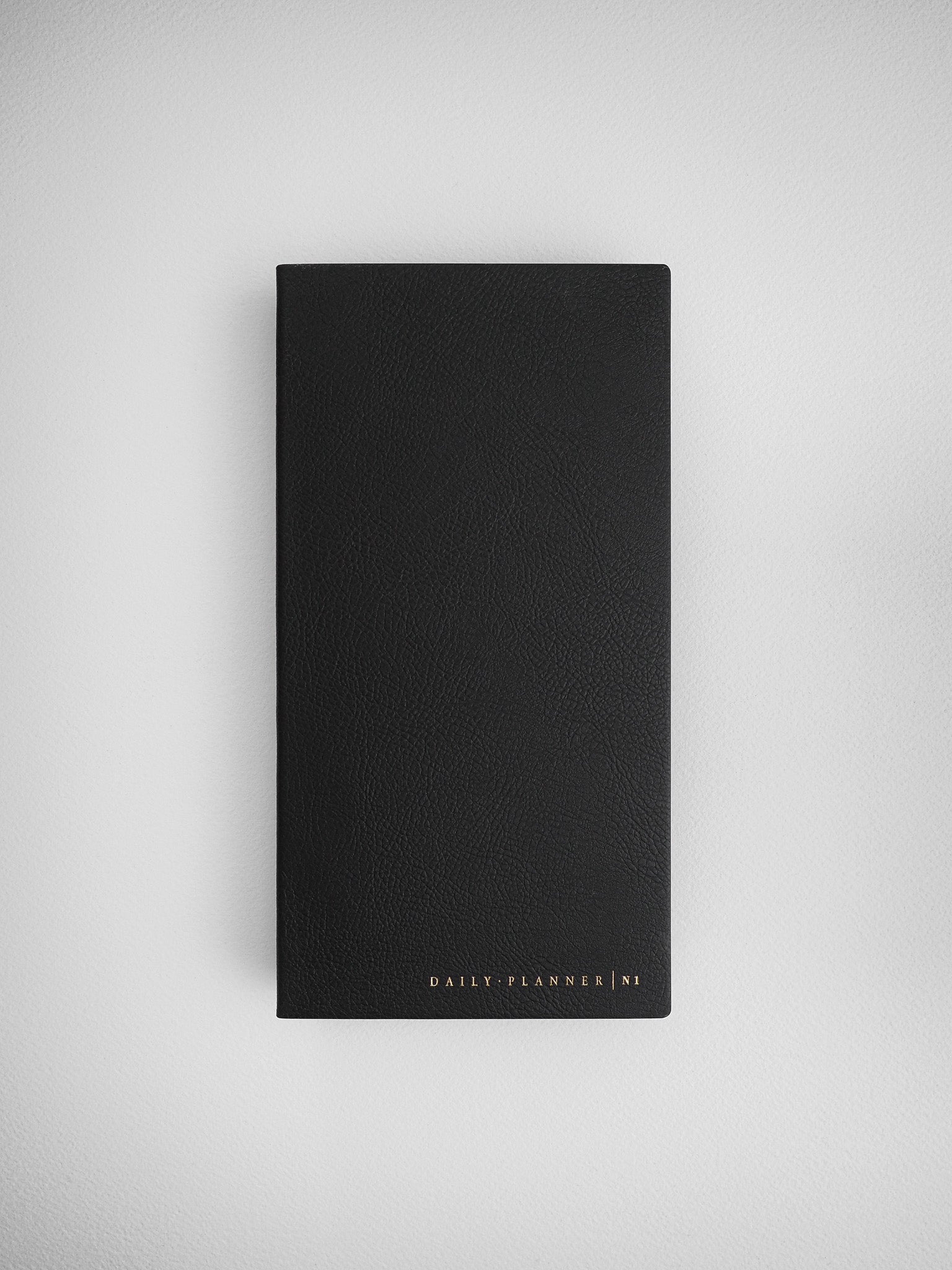 Minimalist black daily planner journal with a smooth faux leather cover and subtle "DAILY PLANNER N1" embossed branding.