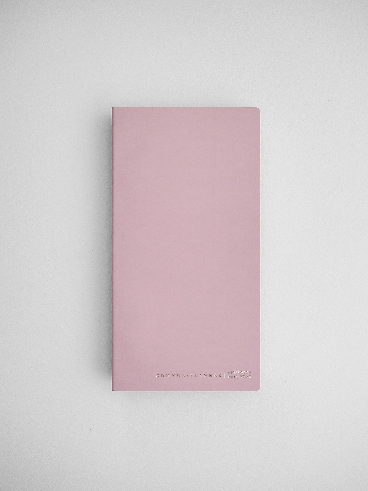 Minimalist blush pink compact planner featuring a soft solid color and subtle "Common Planner" branding, perfect for undated journaling or organization.