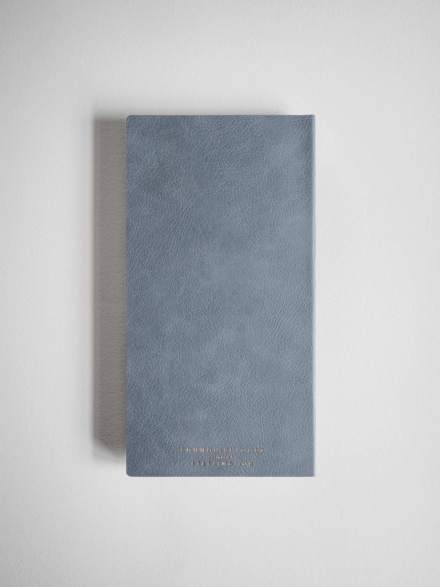 Elegant compact planner with a textured, dusty blue-gray cover and subtle embossed branding near the bottom.