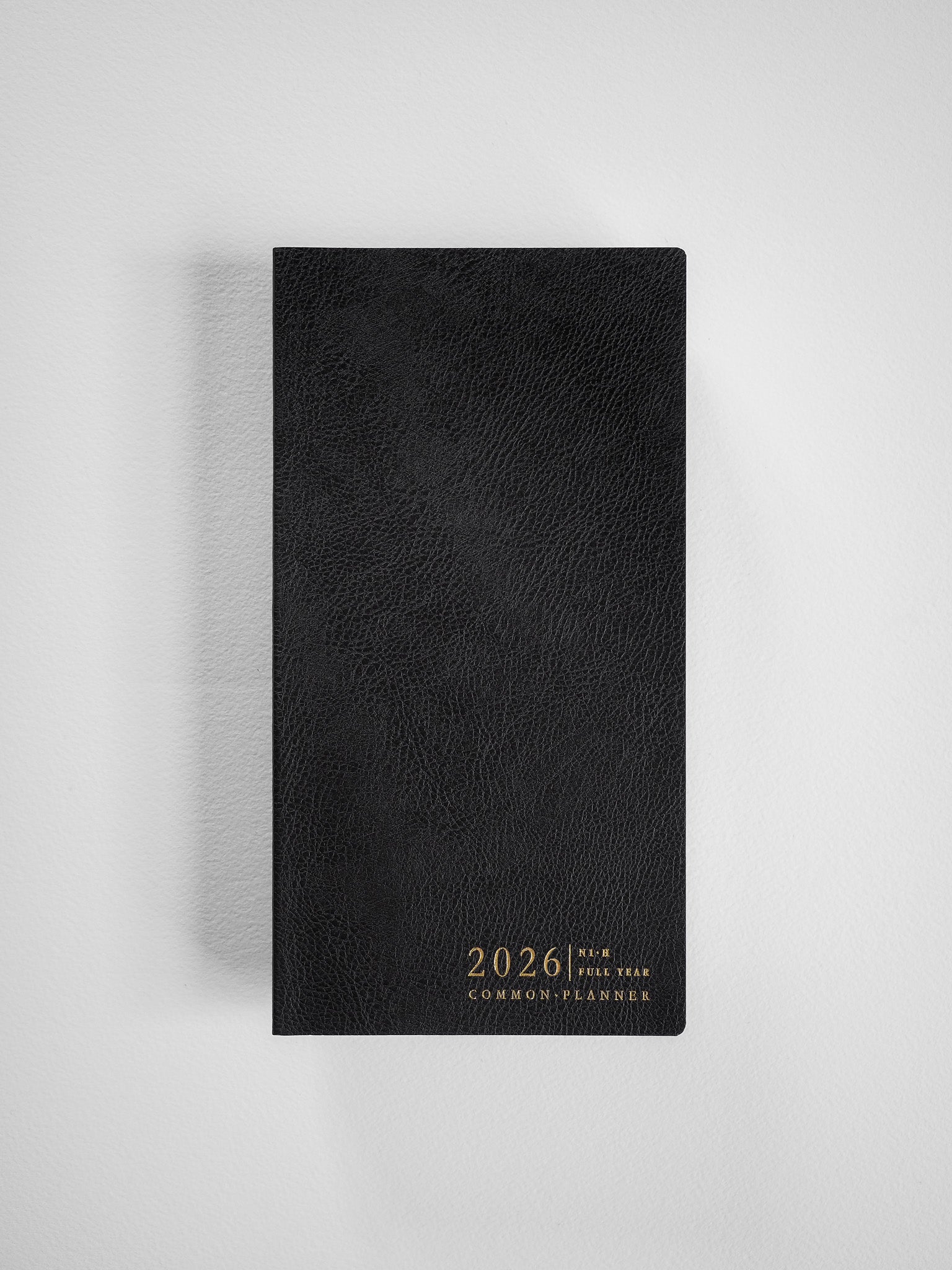 Elegant black planner with a textured faux-leather cover, featuring metallic gold centered text that reads "2026 Full Year Common Planner."