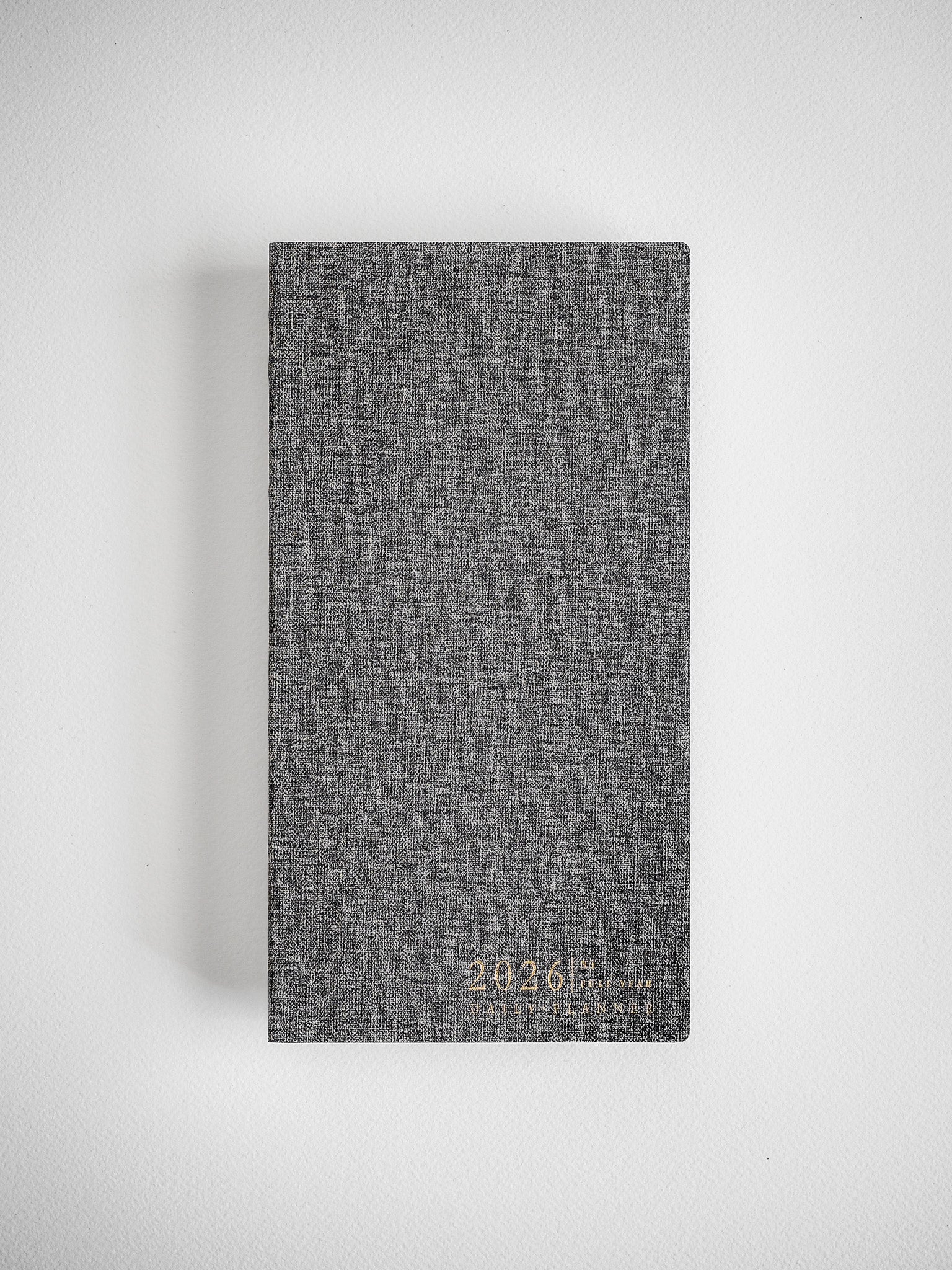 Deep charcoal gray planner with a textured linen cover, subtly embossed with the year 2026, ready for daily scheduling.