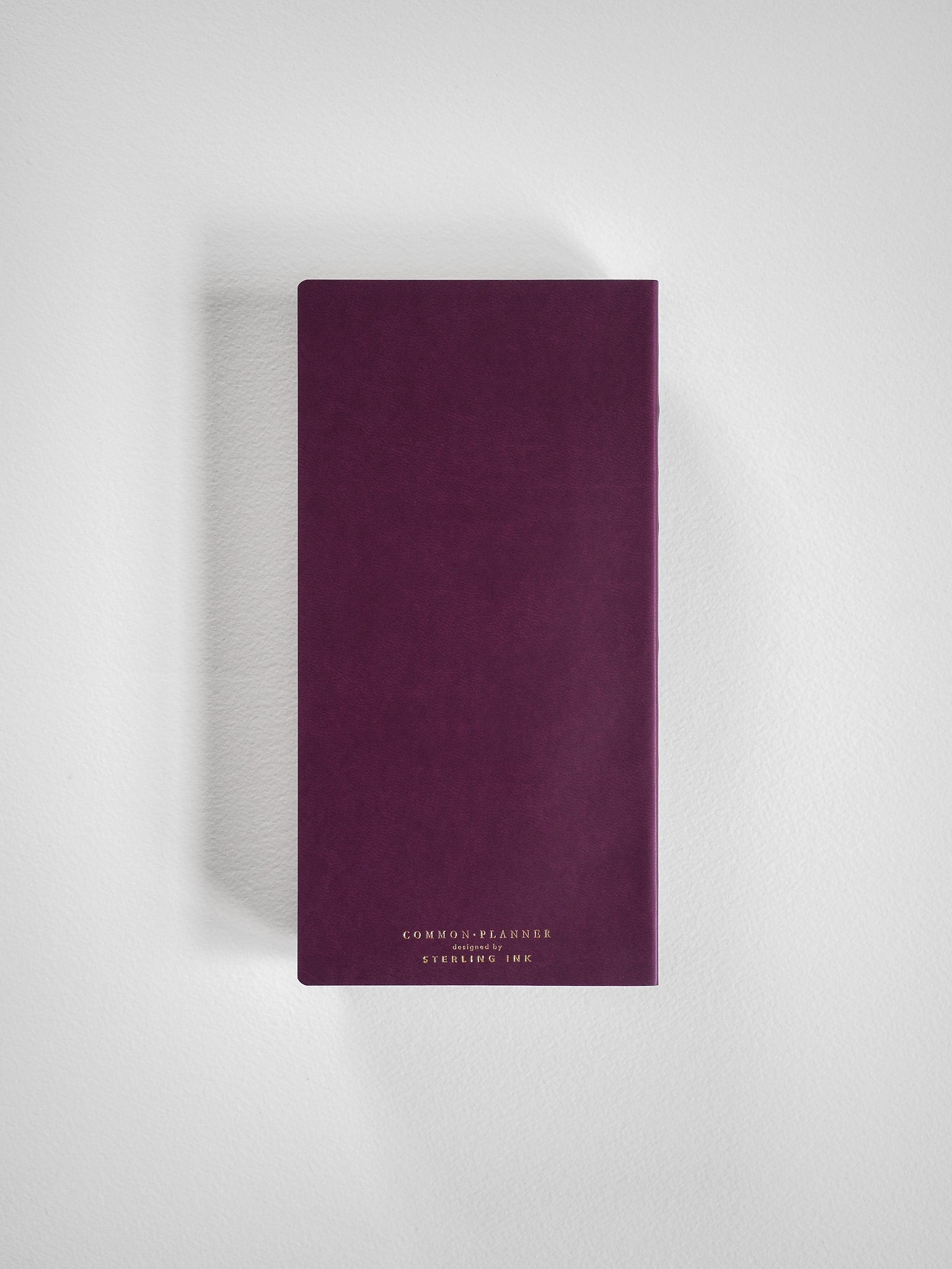 Deep plum-colored 2026 common planner book featuring minimalist gold foil text that reads "COMMON PLANNER" and "STERLING INK."