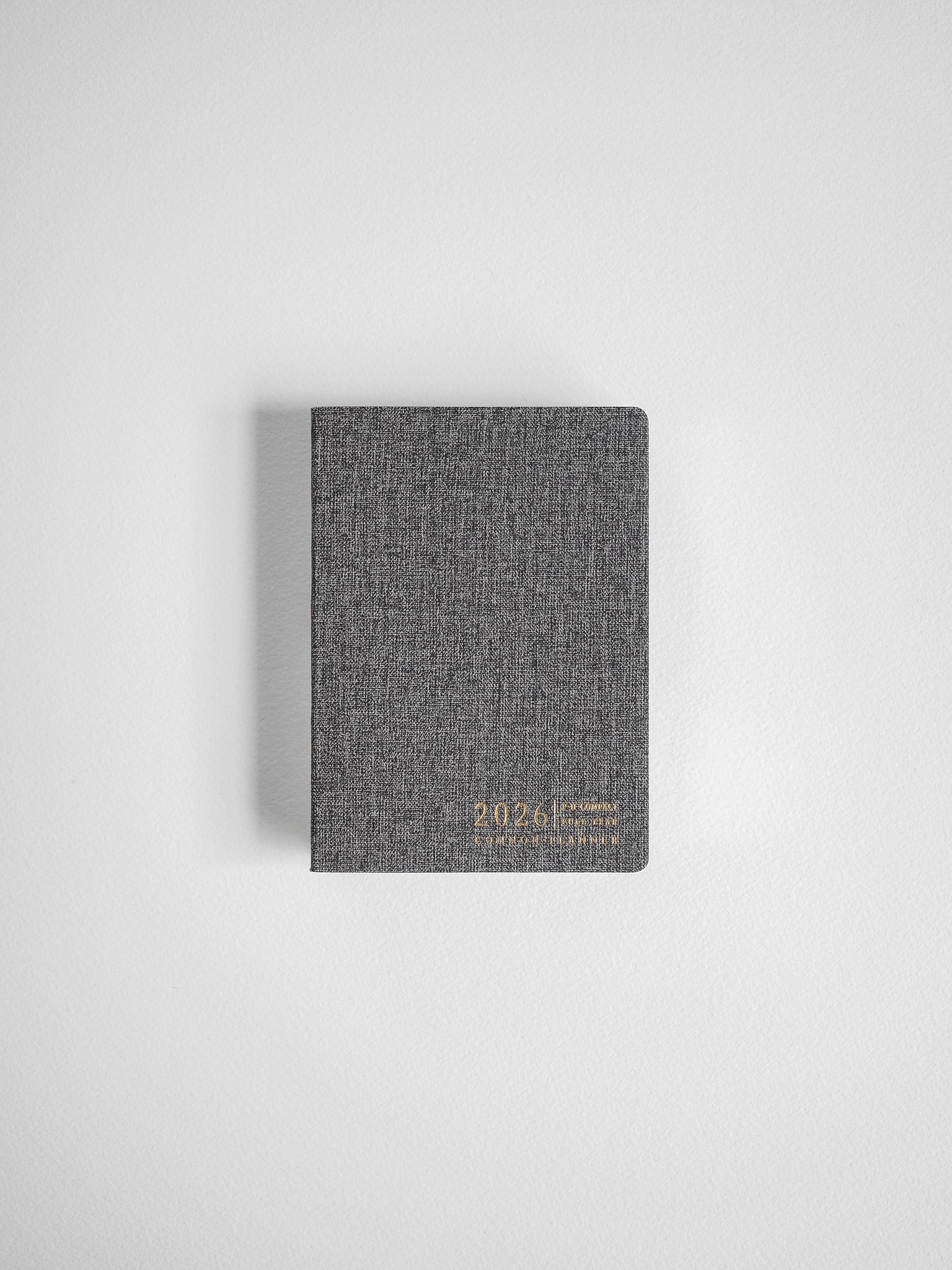 Compact, dark charcoal gray annual planner featuring a textured cover and clear 2026 inscription for full-year organization.