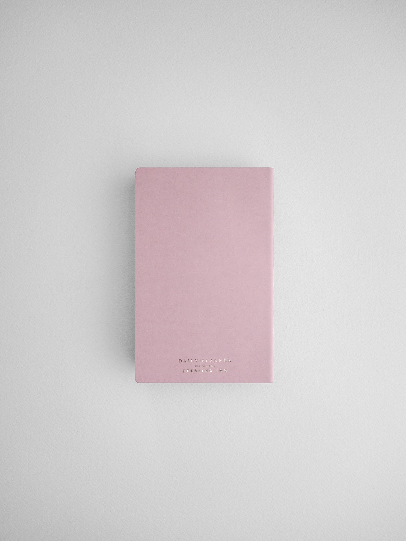 Minimalist blush pink daily planner notebook featuring black lettering and a clean, modern design for journaling or scheduling.