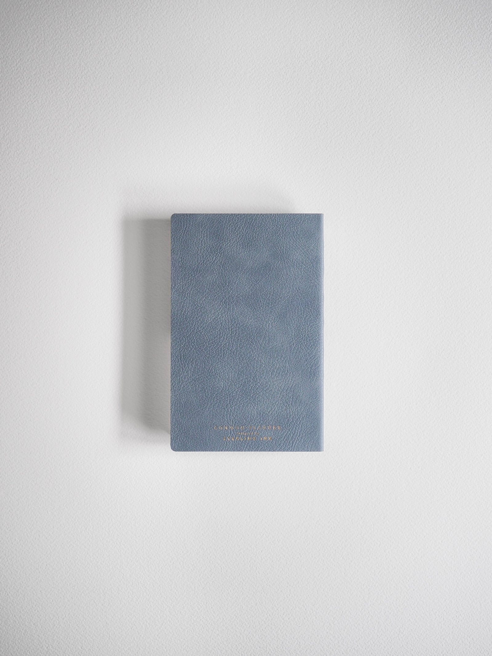 Compact, dusty blue-gray planner with a smooth, minimalist cover and light embossed lettering detailing the full-year schedule.