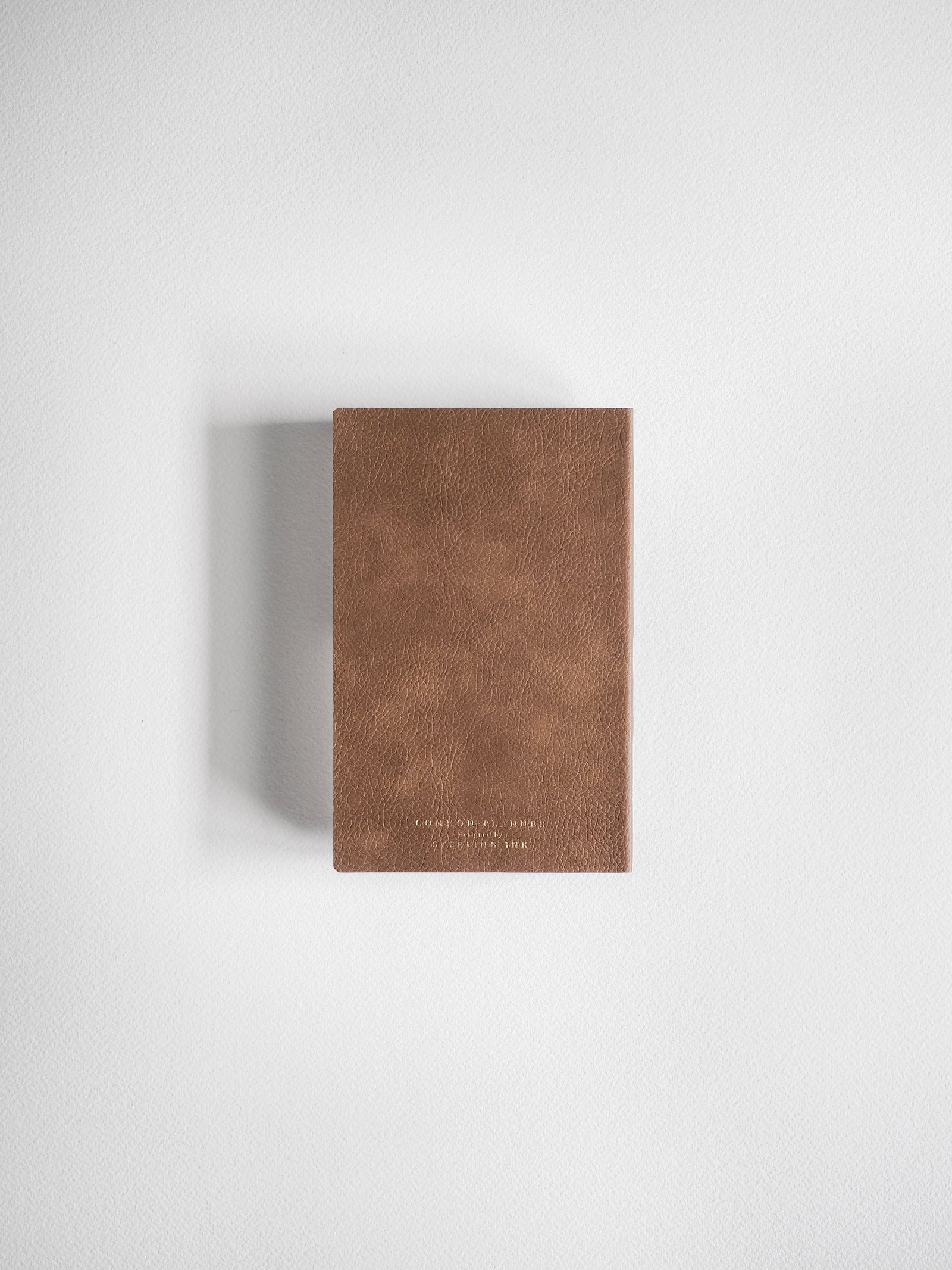 A vertical pocket planner crafted from textured, reddish-brown faux leather, featuring subtle gold debossing on the front cover.
