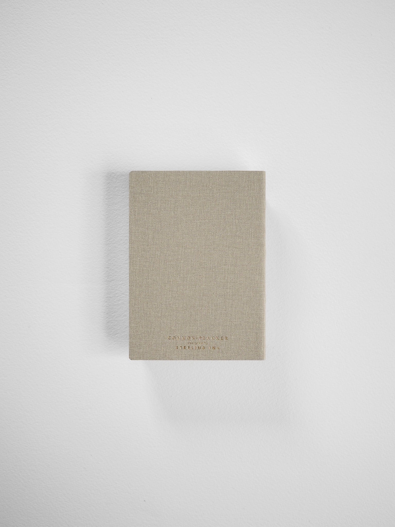 Compact, vertical planner in a natural beige linen texture, featuring minimalist, debossed branding suitable for comprehensive 2026 year organization.