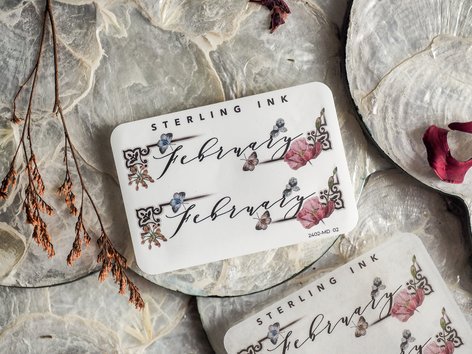 Ornate white sticker reading 'February' featuring romantic, hand-painted floral accents in blush pink, deep red, and muted blue ink.
