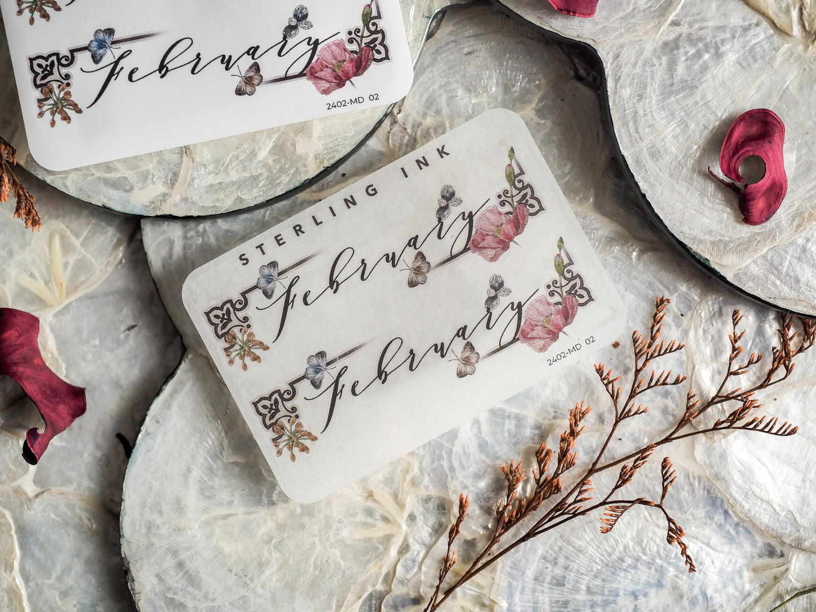 Decorative month sticker for February, featuring the word in elegant script and adorned with delicate, hand-drawn watercolor clusters of pink, blue, and burgundy florals.