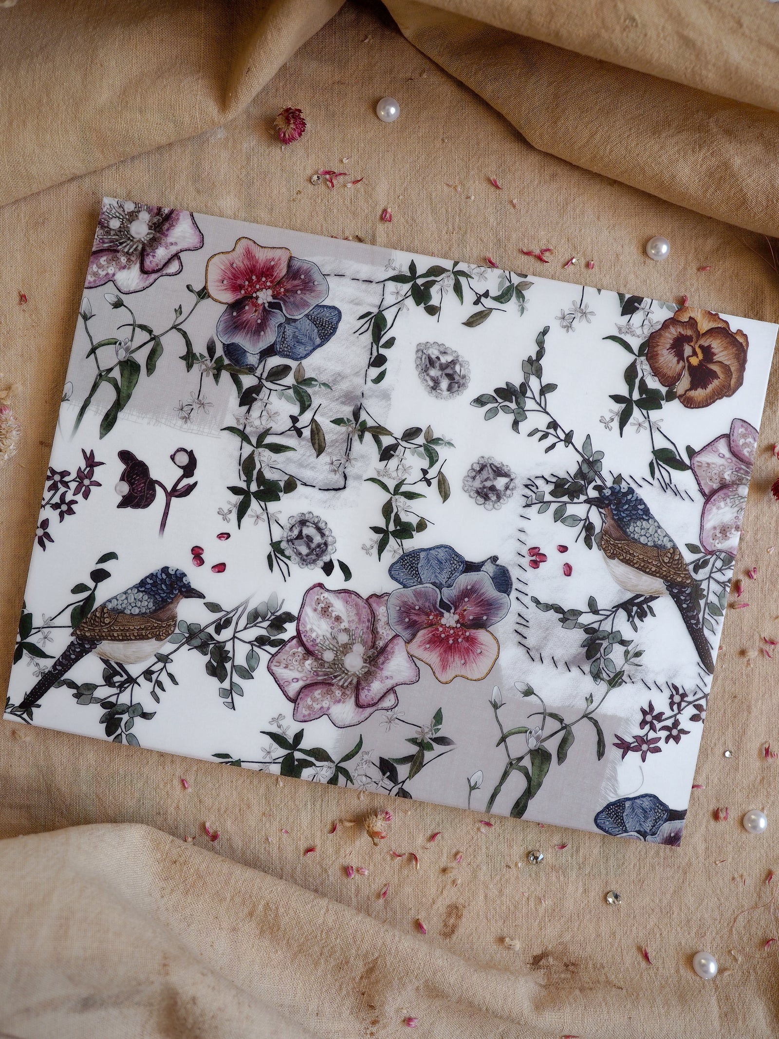 Elegant botanical print featuring watercolor flowers, lush foliage, and small birds, rendered in soft dusty purples and mauves.