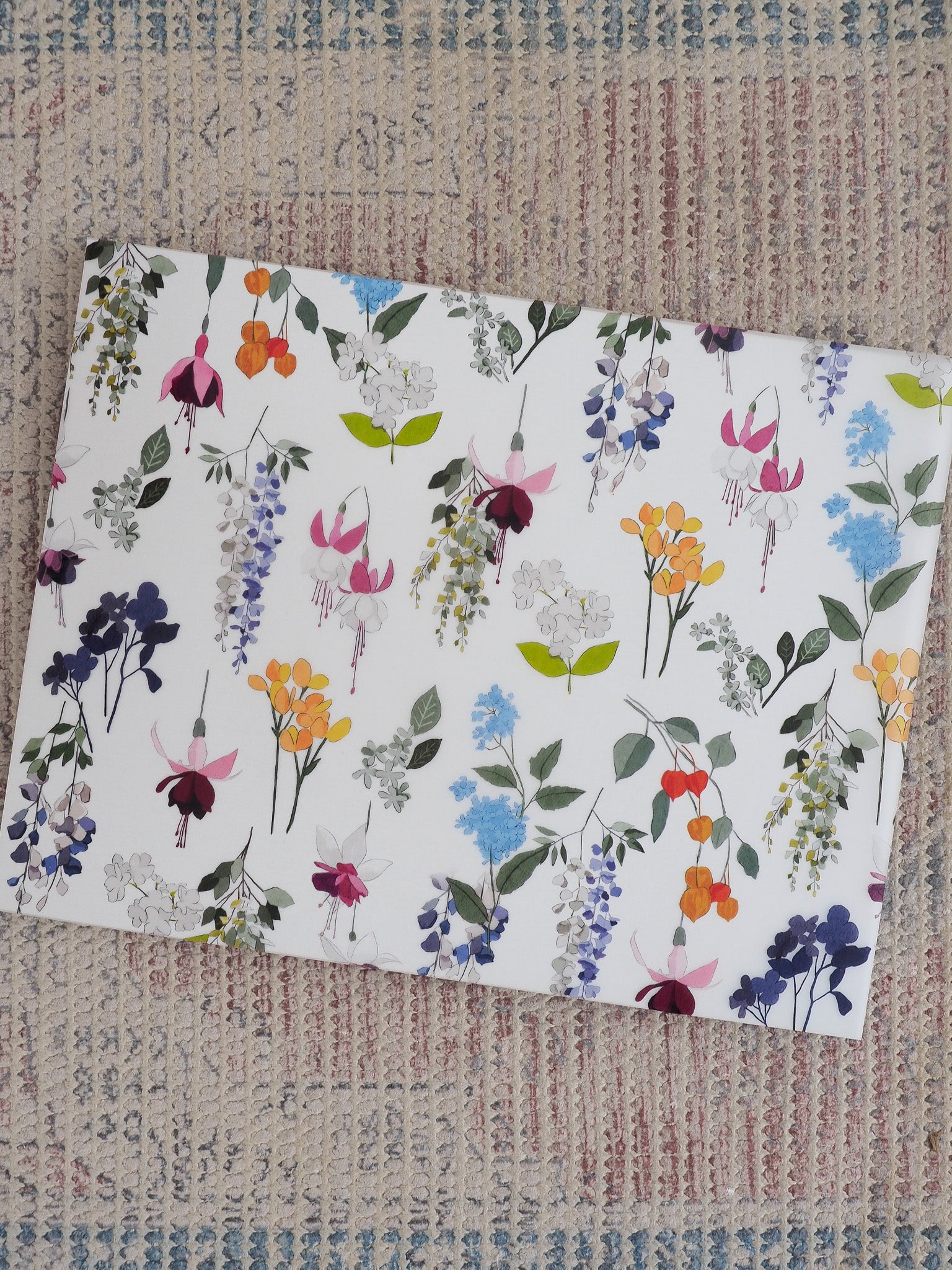 Vibrant watercolor floral pattern covering a planner, featuring abundant spring blossoms and greenery in delicate shades of lavender, blue, yellow, orange, and purple.