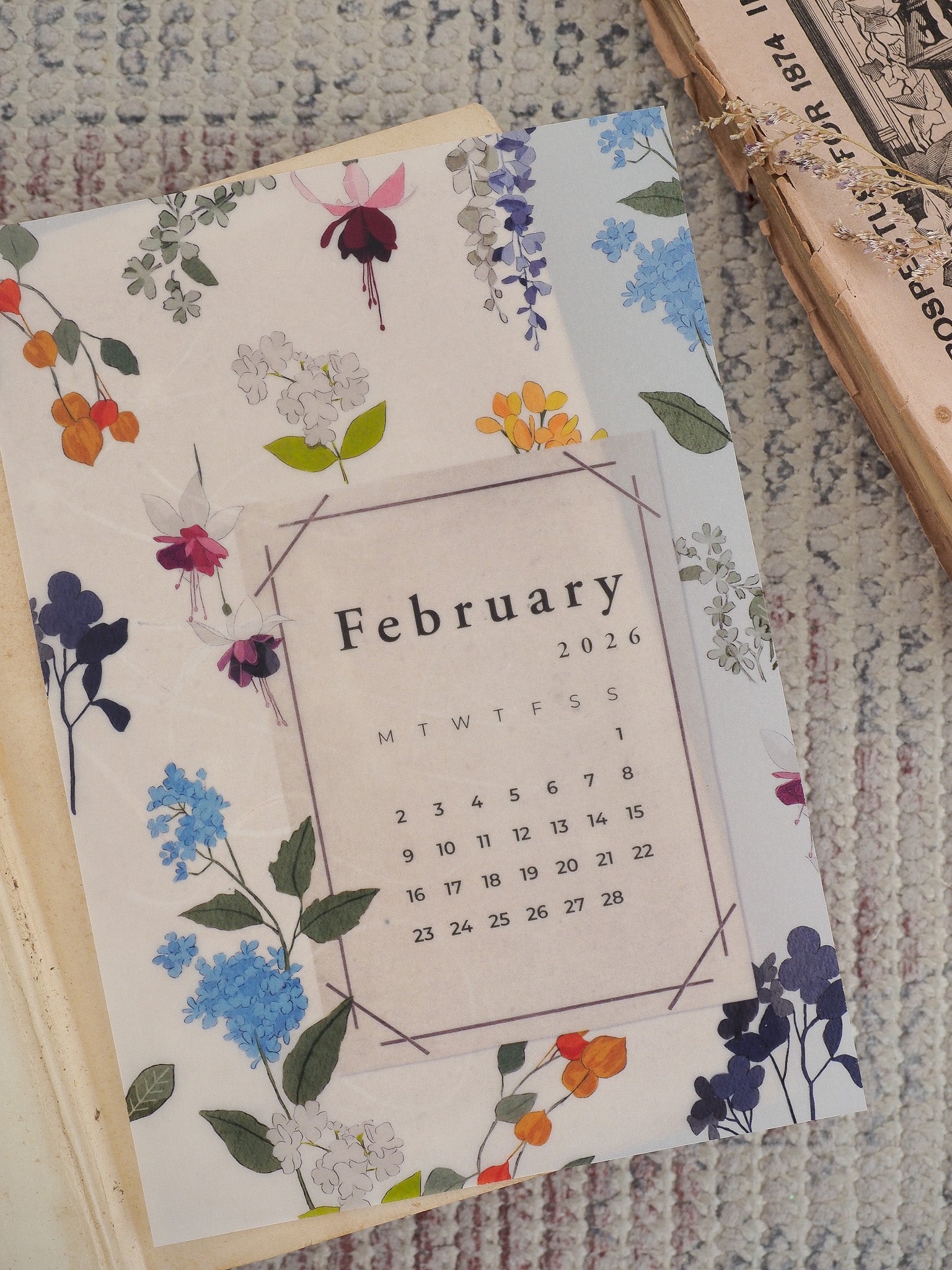 Watercolor floral calendar for February 2026, featuring a sweet pattern of blue, purple, and cream blooms surrounding the month grid.