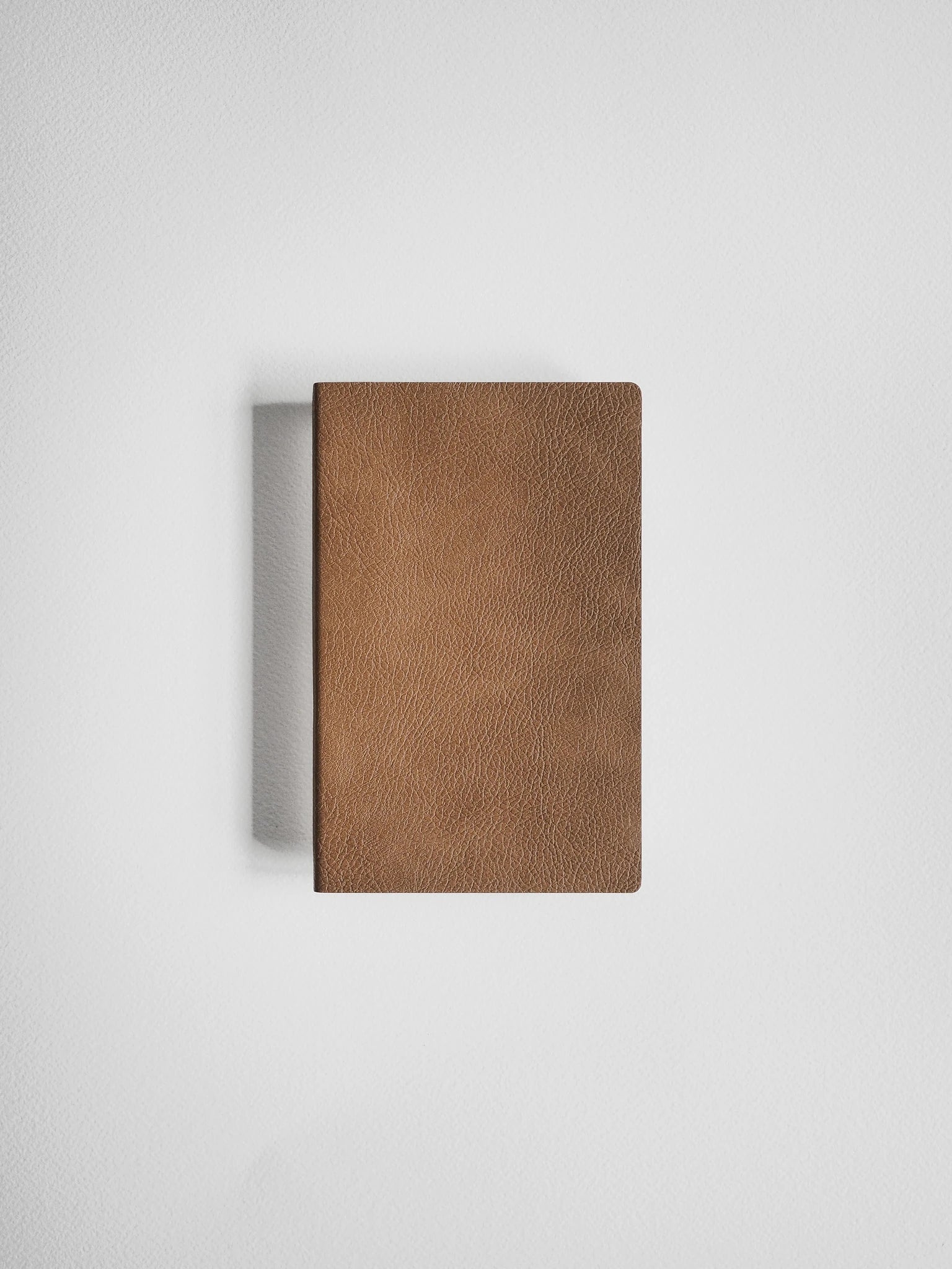 A brown textured leather notebook or journal with a pebbled leather cover, shown closed against a neutral light gray background.
#Color_Caramel