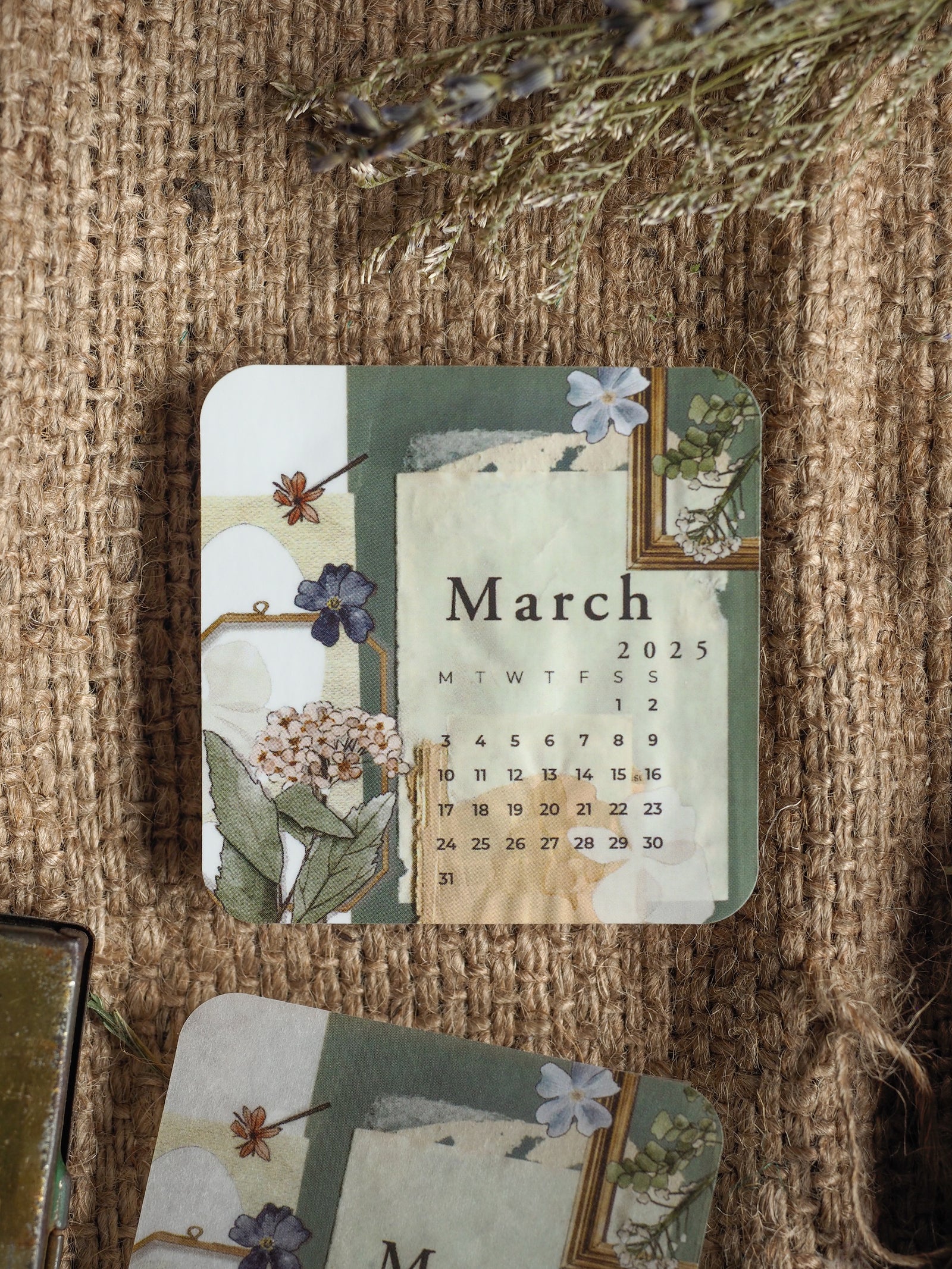 A delicate, vintage floral calendar sticker for March 2025 featuring a muted palette of watercolor greenery and small blue blossoms.