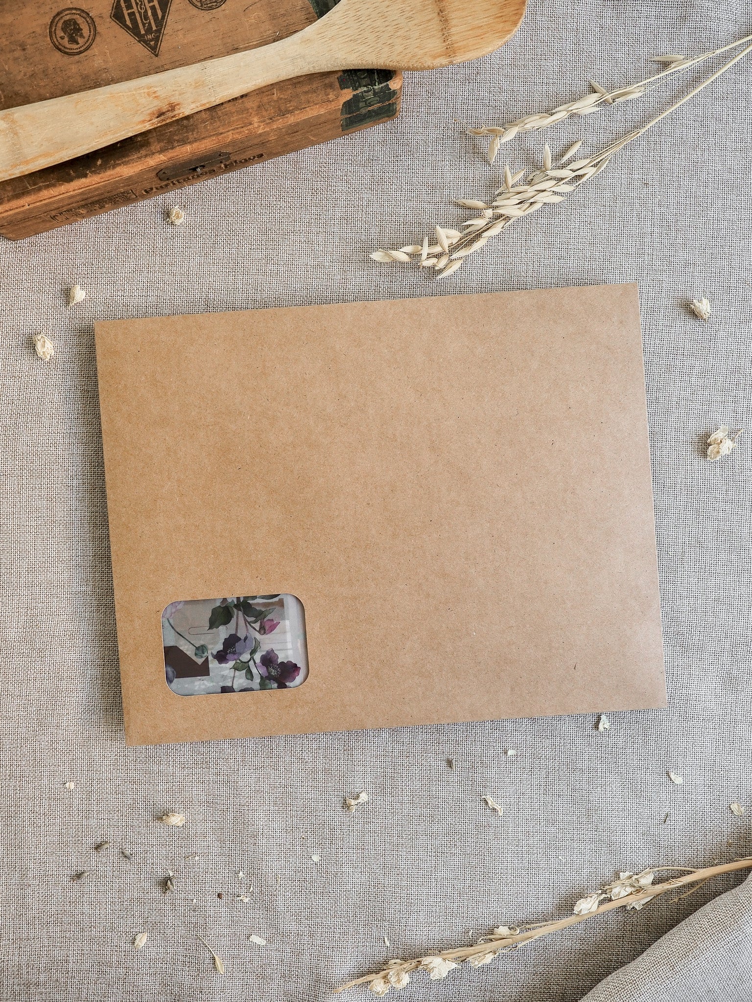 Rustic kraft paper envelope holding a delicate floral insert featuring purple and muted spring blossoms for the March 2026 kit.